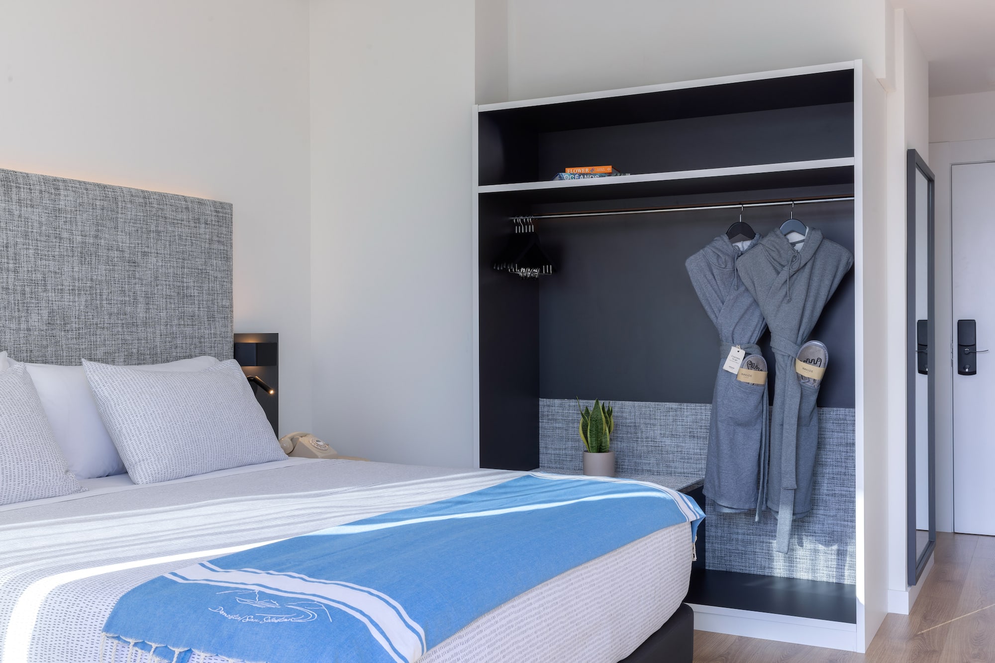 Dormitorio hotel moderno: cama, manta azul y armario con batas.