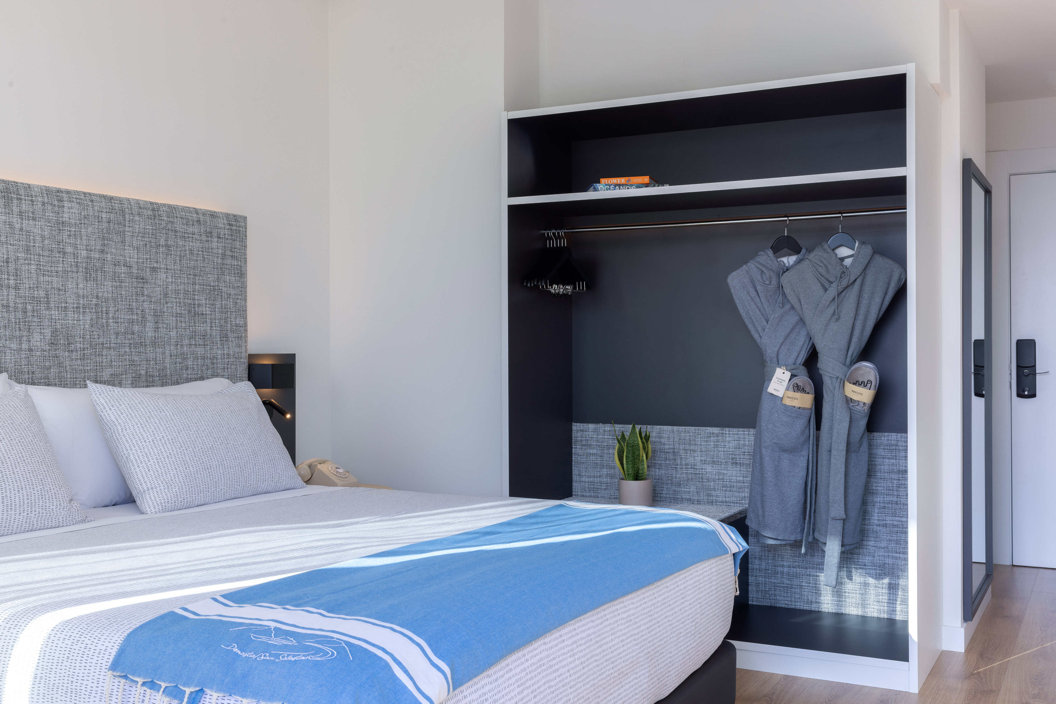 Dormitorio hotel moderno: cama, manta azul y armario con batas.