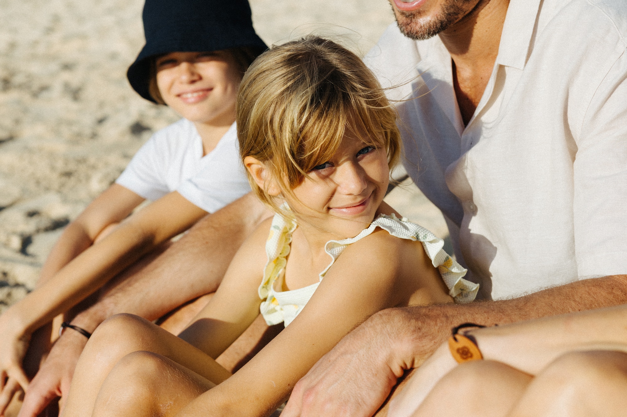 Dad, daughter, son smiling together on a sandy beach.