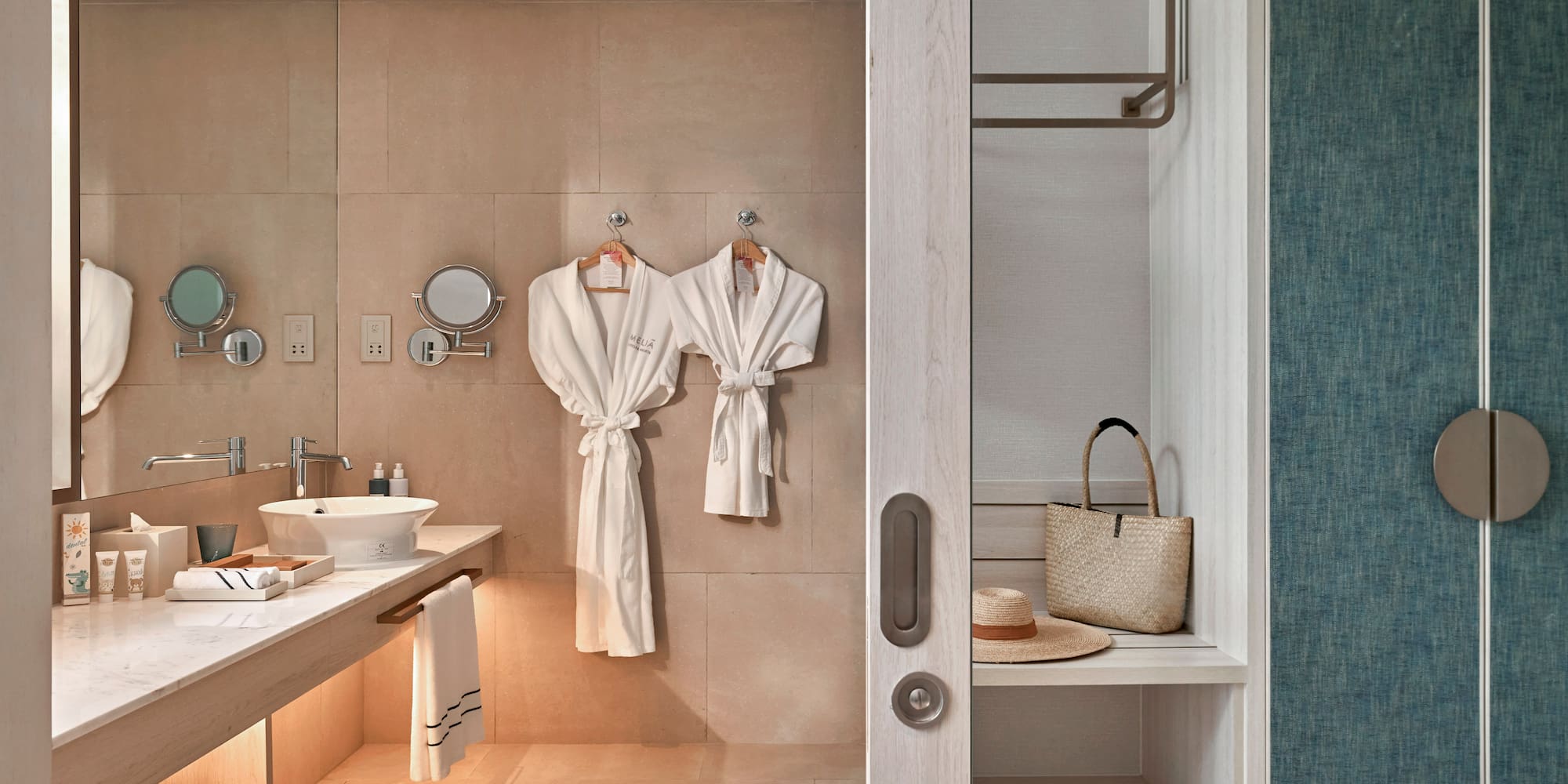 Hotel bathroom with vanity, white bathrobes, and adjacent closet storage.