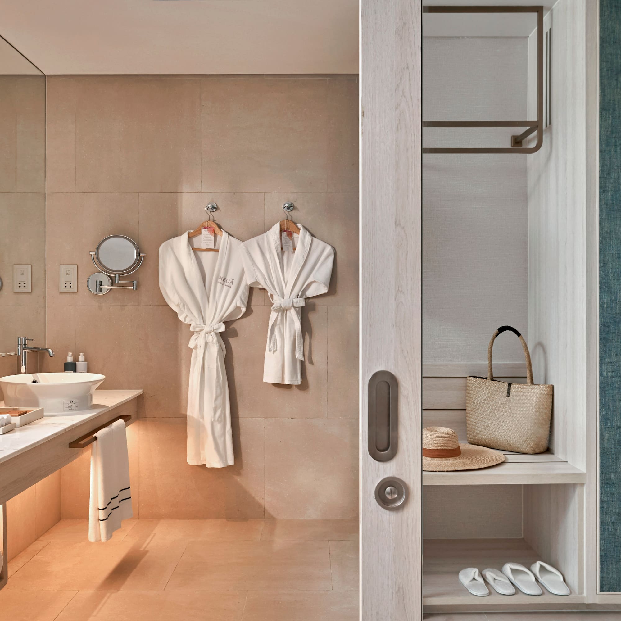 Hotel bathroom with vanity, white bathrobes, and adjacent closet storage.
