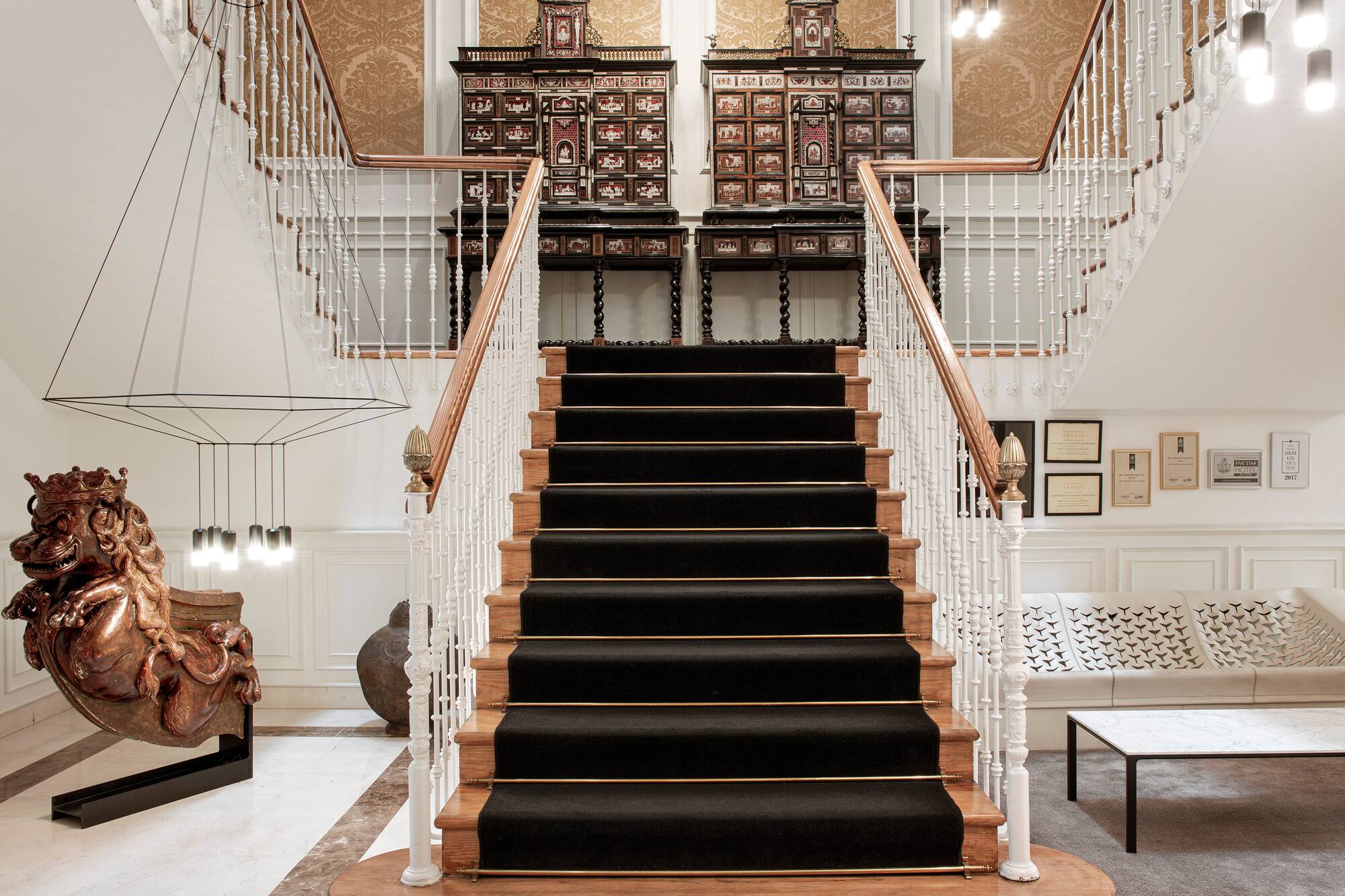 Hotel lobby grand staircase with black runner and ornate antique cabinets.