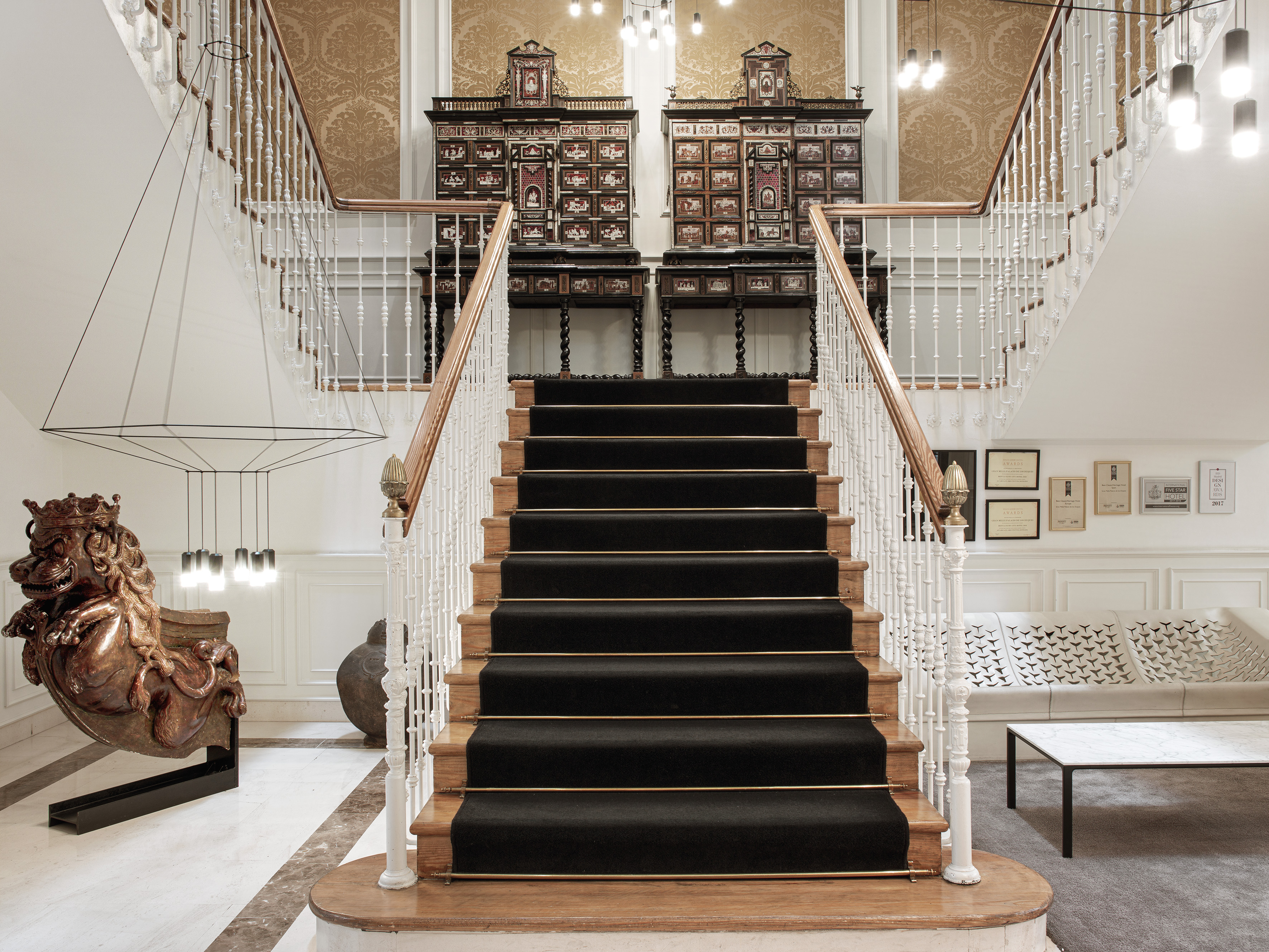 Hotel lobby grand staircase with black runner and ornate antique cabinets.