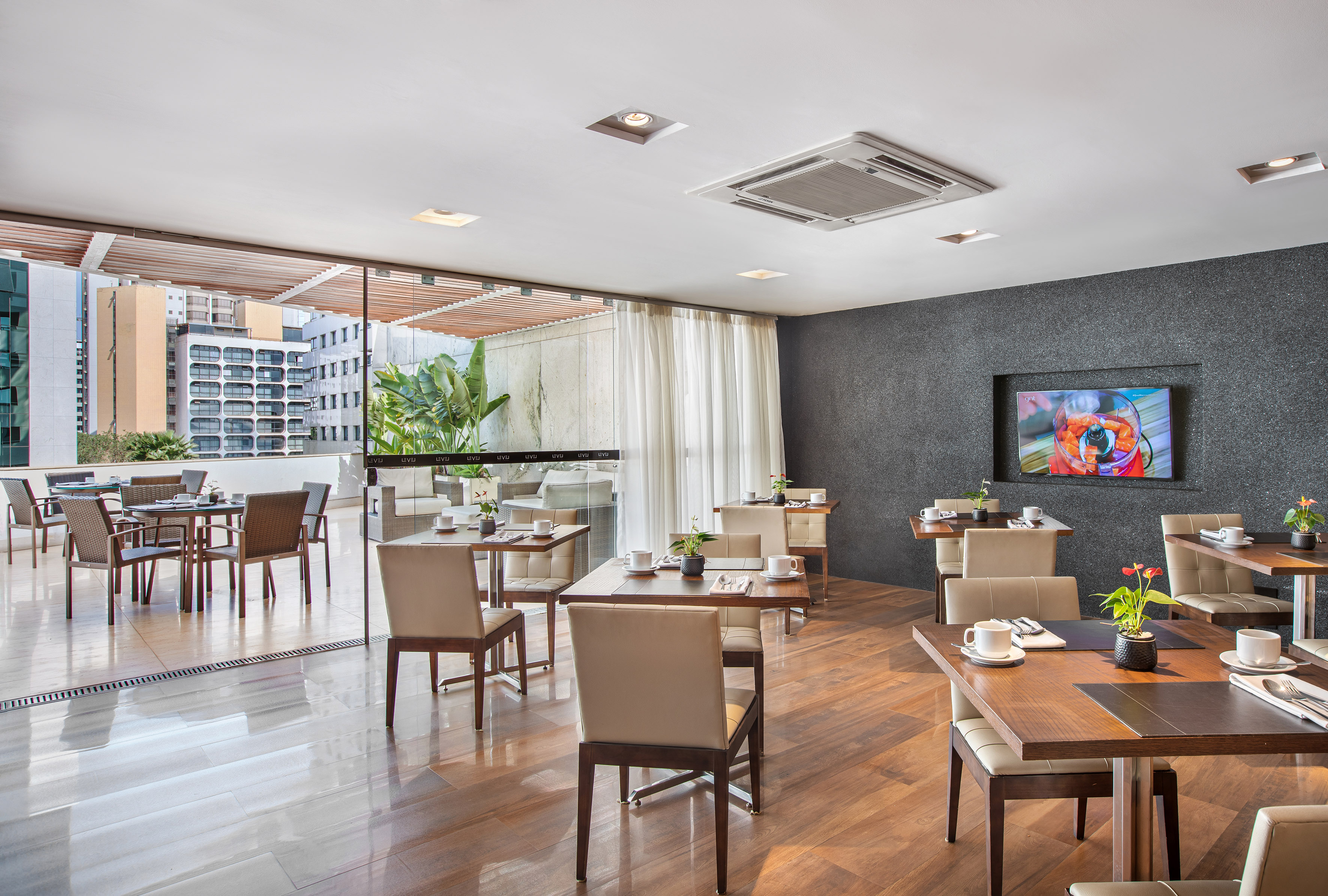 Modern restaurant dining area with set tables, city view, and wood flooring.
