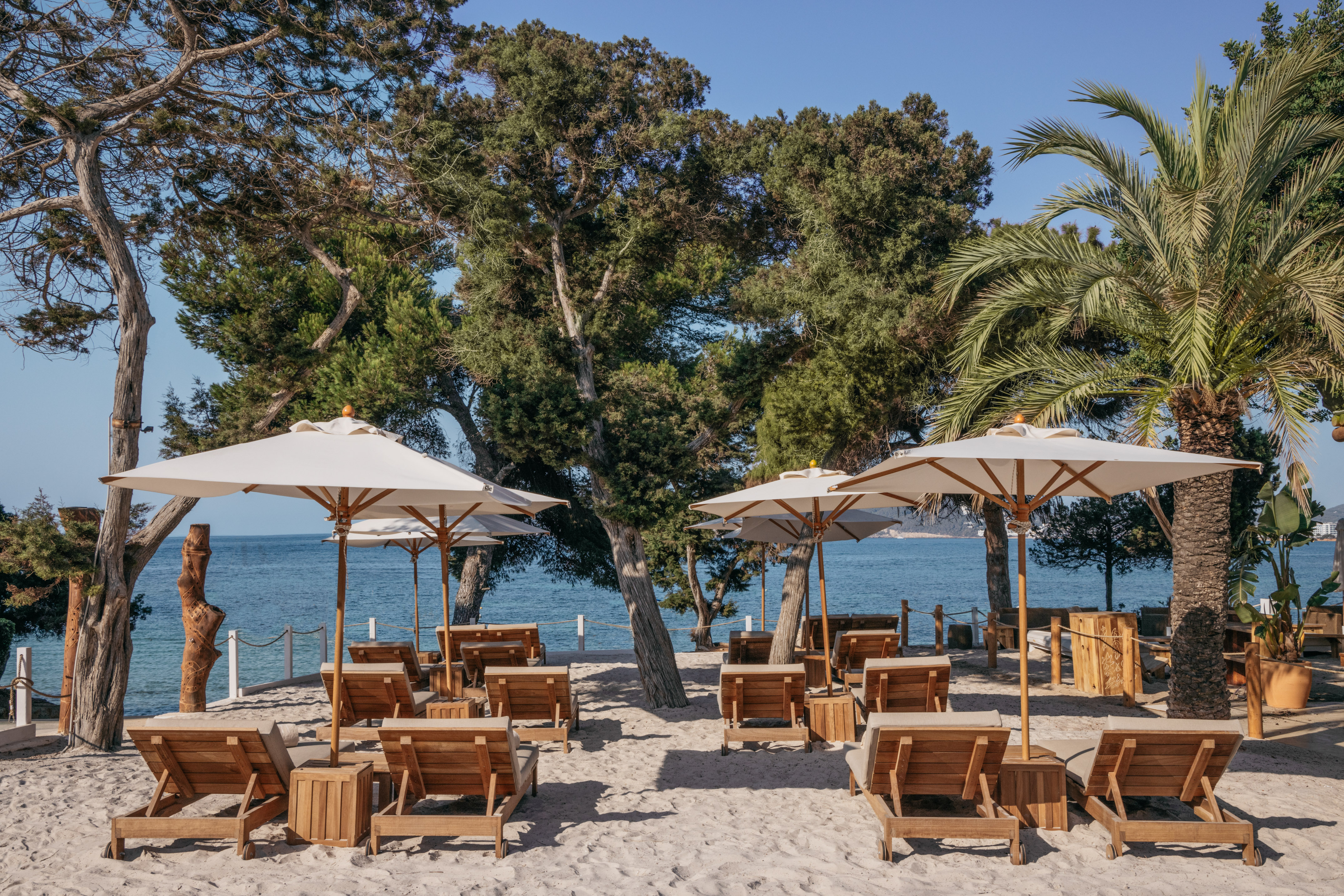 Sunny sandy beach with wooden lounge chairs, umbrellas, and blue sea.