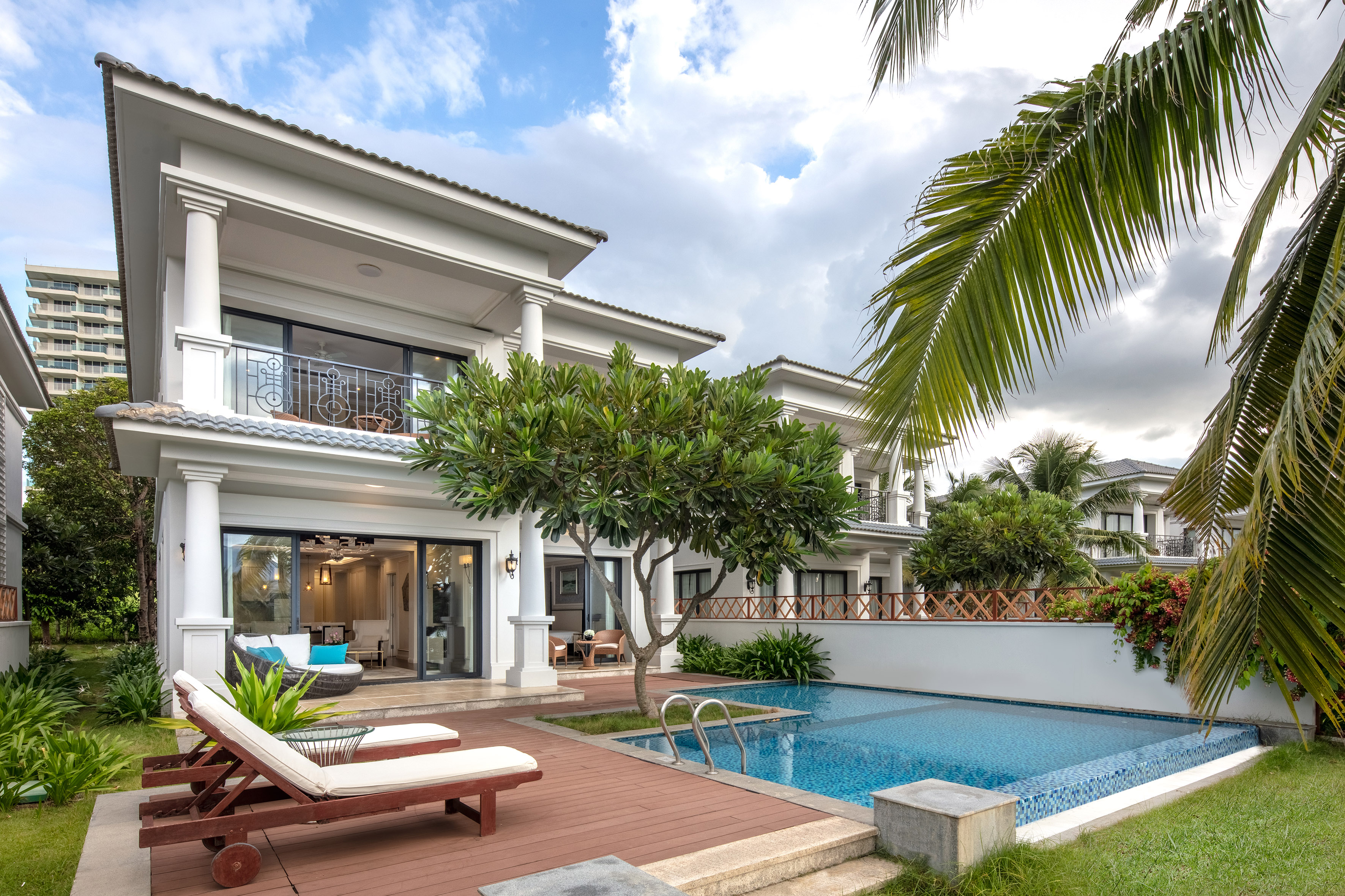 White villa, private pool, wooden deck with lounge chairs, and tropical palm trees.