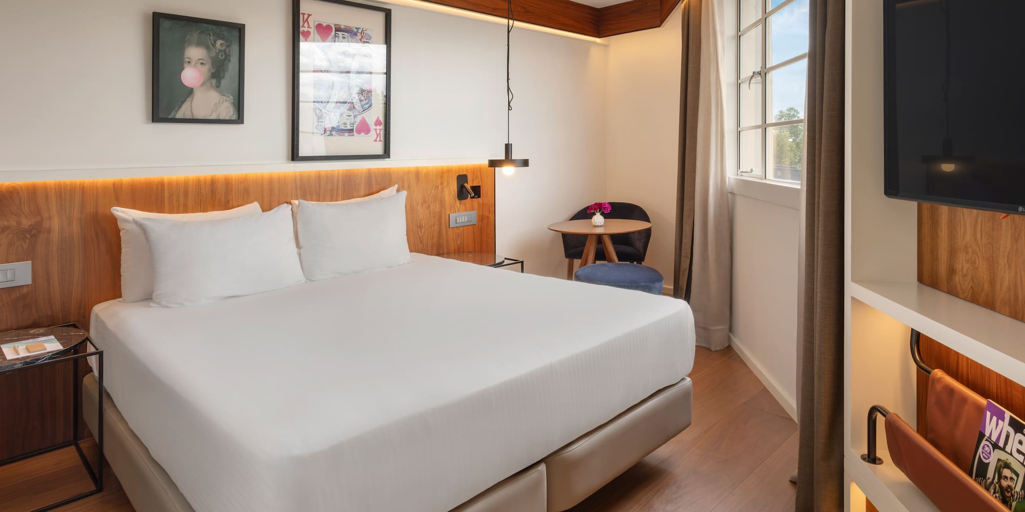 Contemporary hotel room with queen bed, wood features, and window.