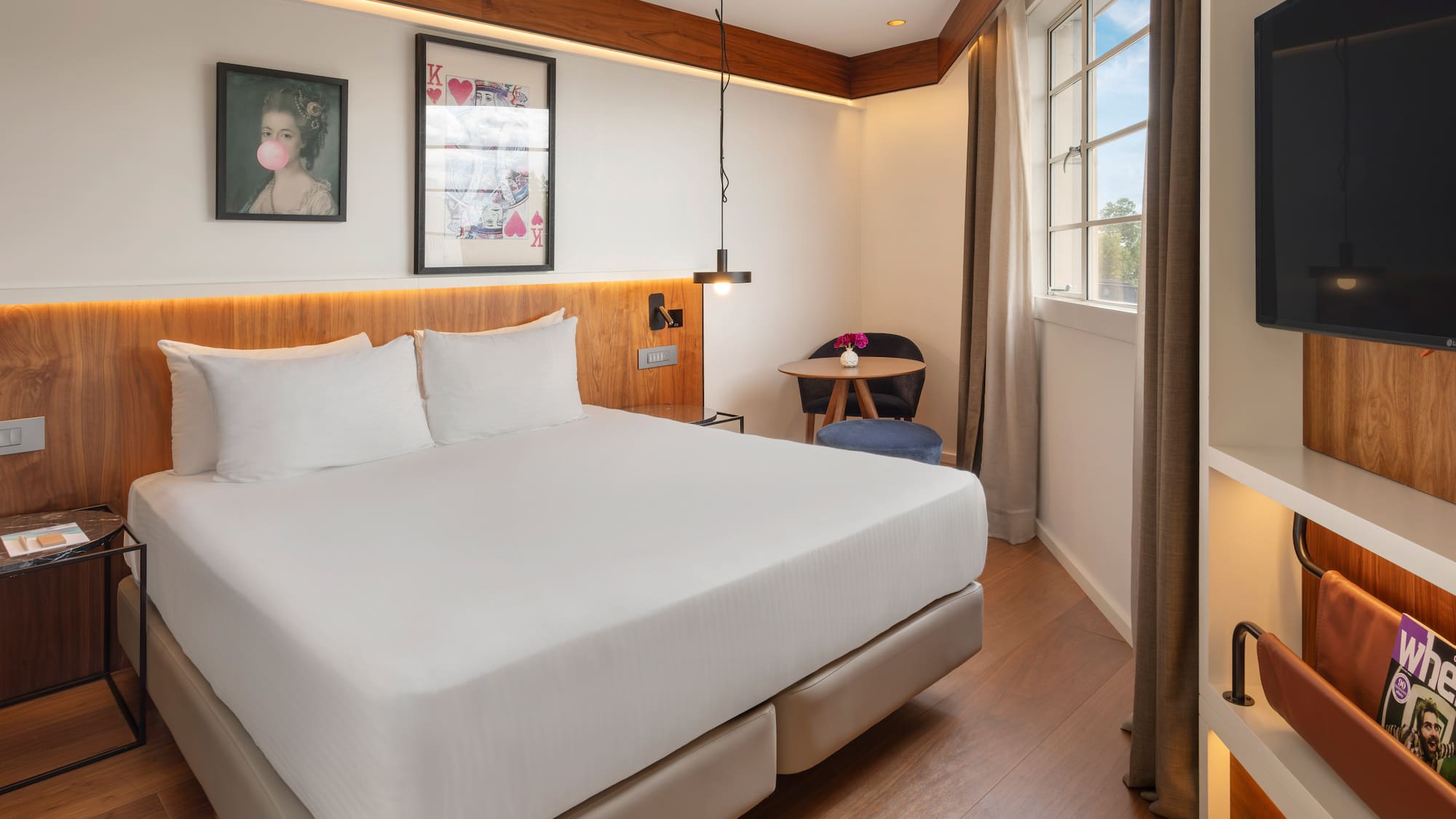 Contemporary hotel room with queen bed, wood features, and window.