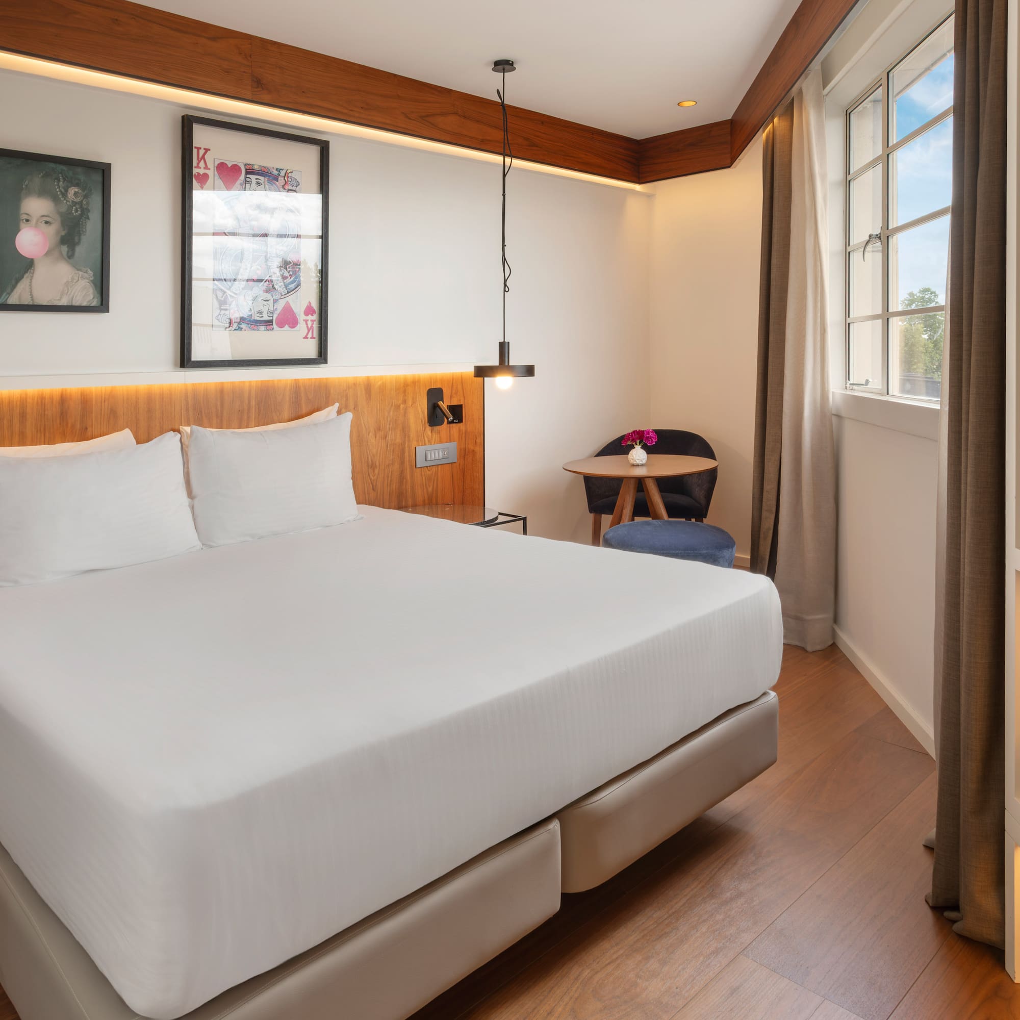 Contemporary hotel room with queen bed, wood features, and window.
