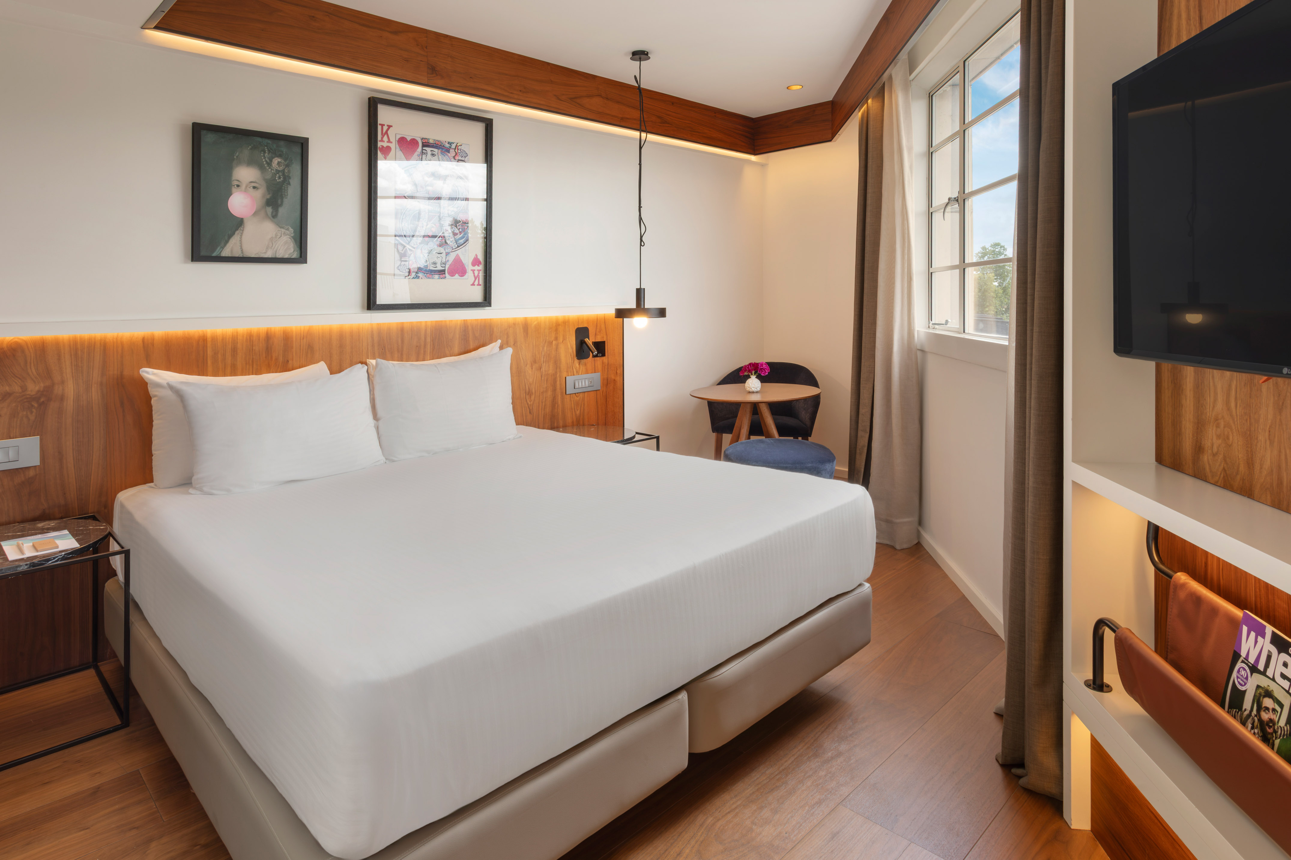 Contemporary hotel room with queen bed, wood features, and window.