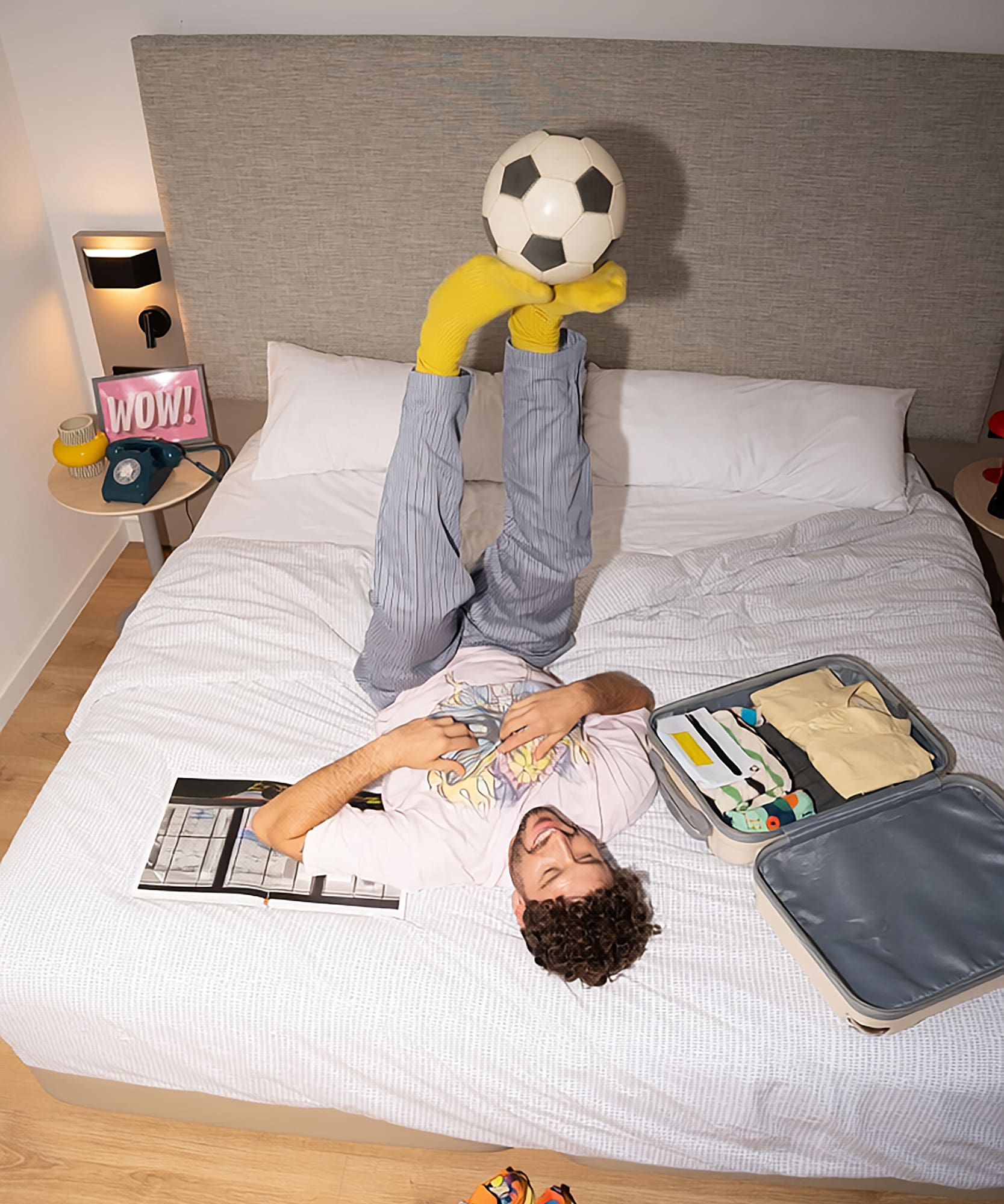a man lying on a bed with his feet up with a football ball