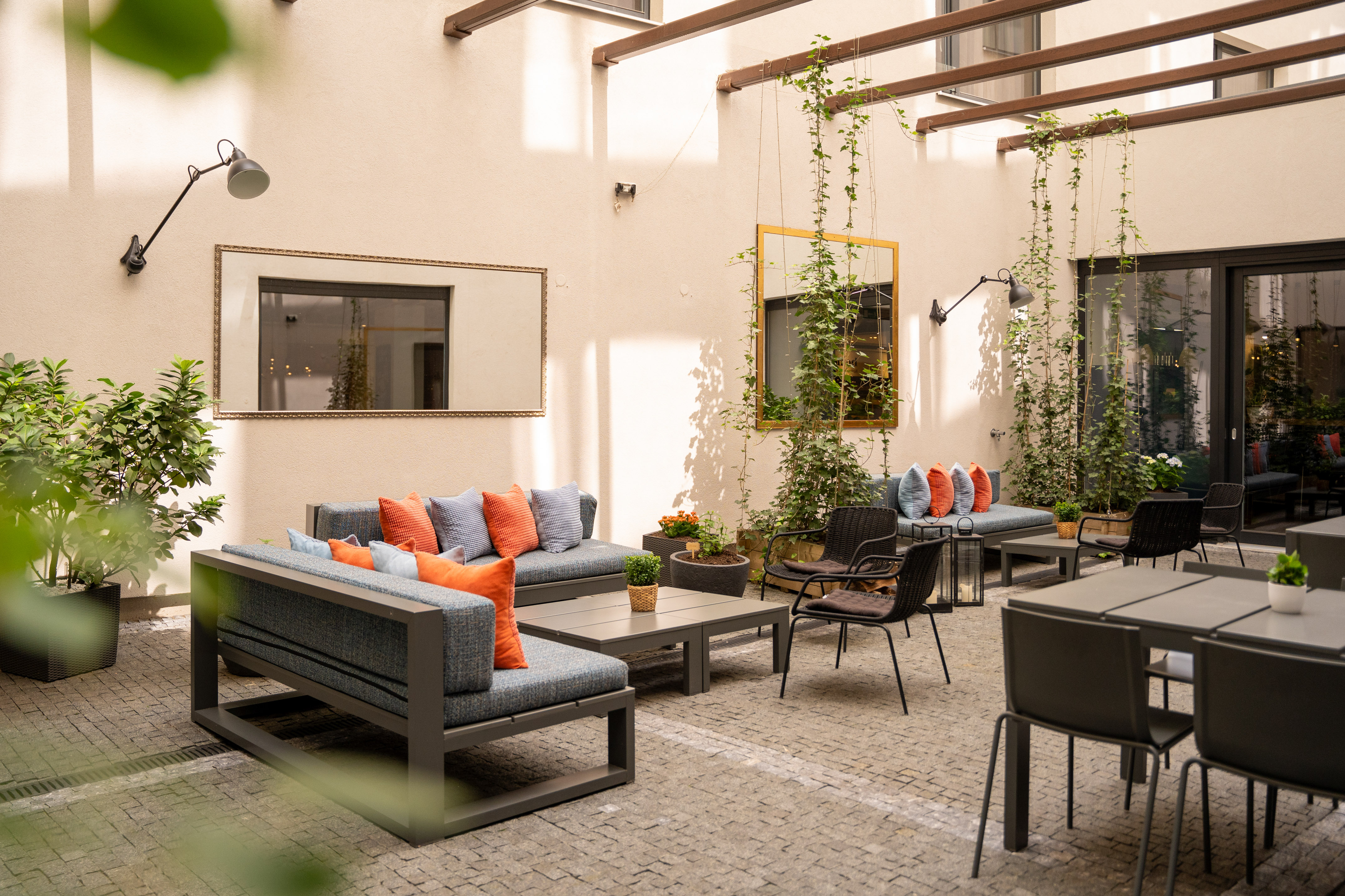 Outdoor patio with comfortable modern seating, orange cushions, and green vines.