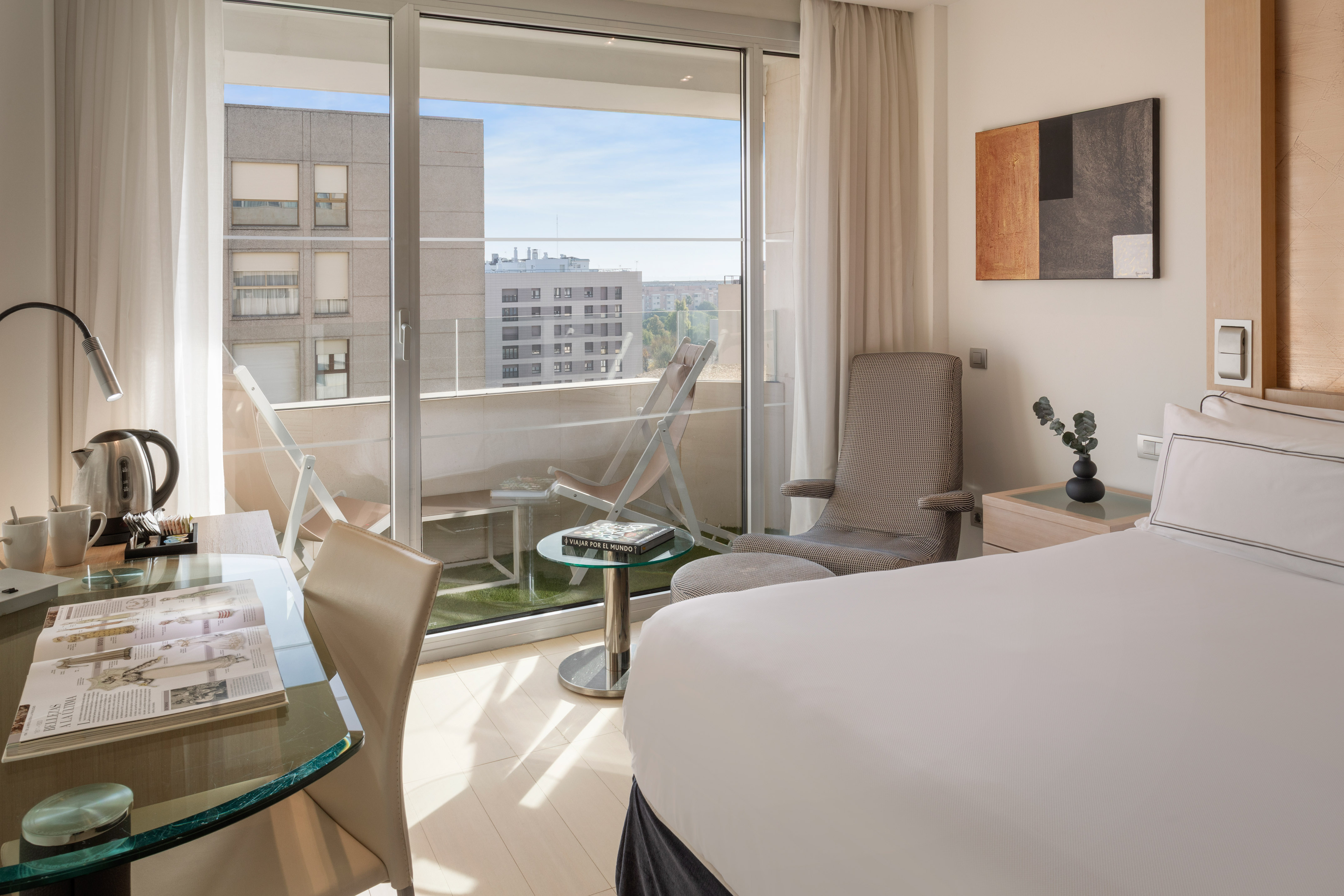 Bright modern hotel room with bed, desk, balcony, and city view.