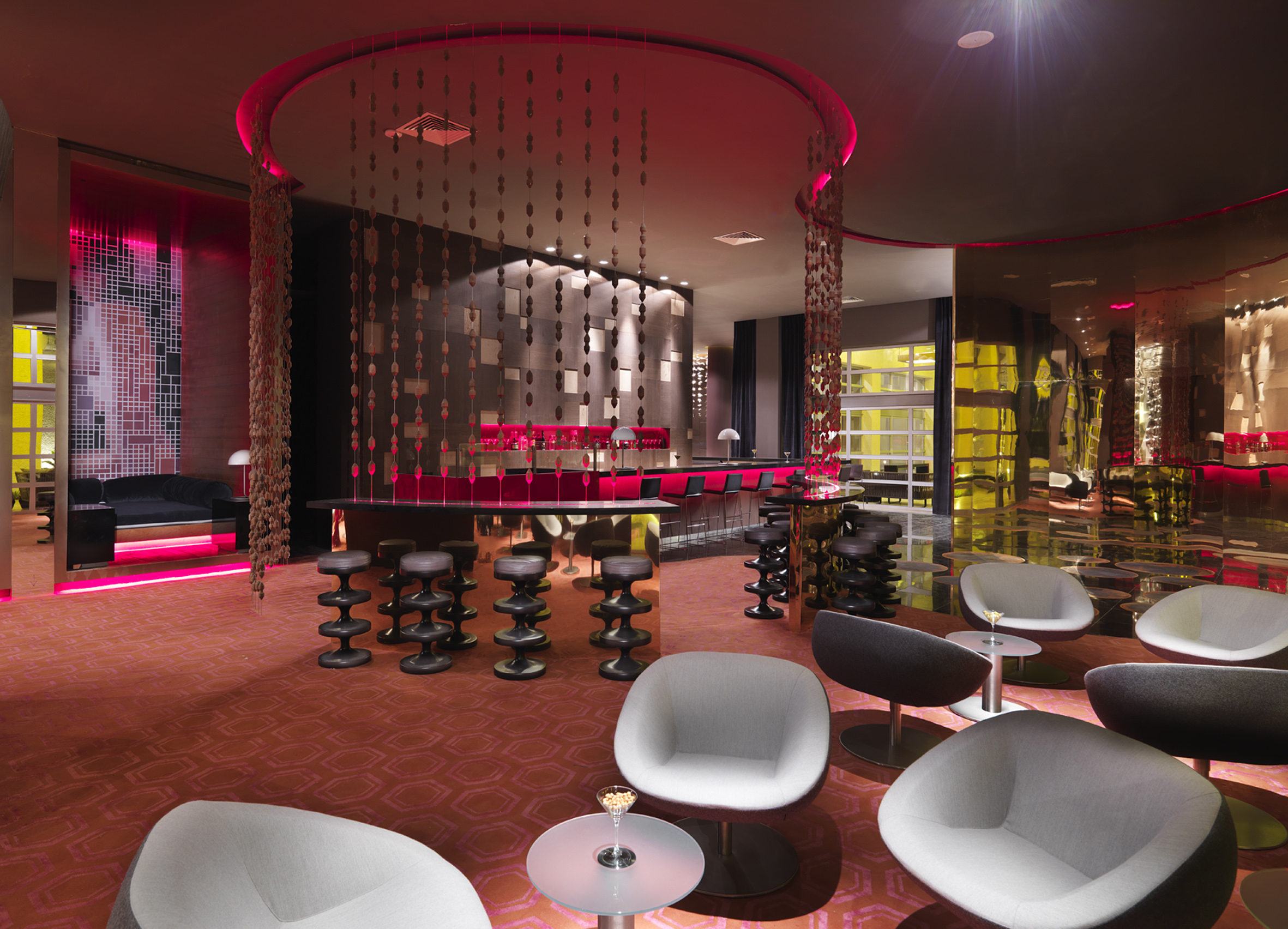 Modern red-lit hotel bar lounge with stylish seating and decorative hangings.