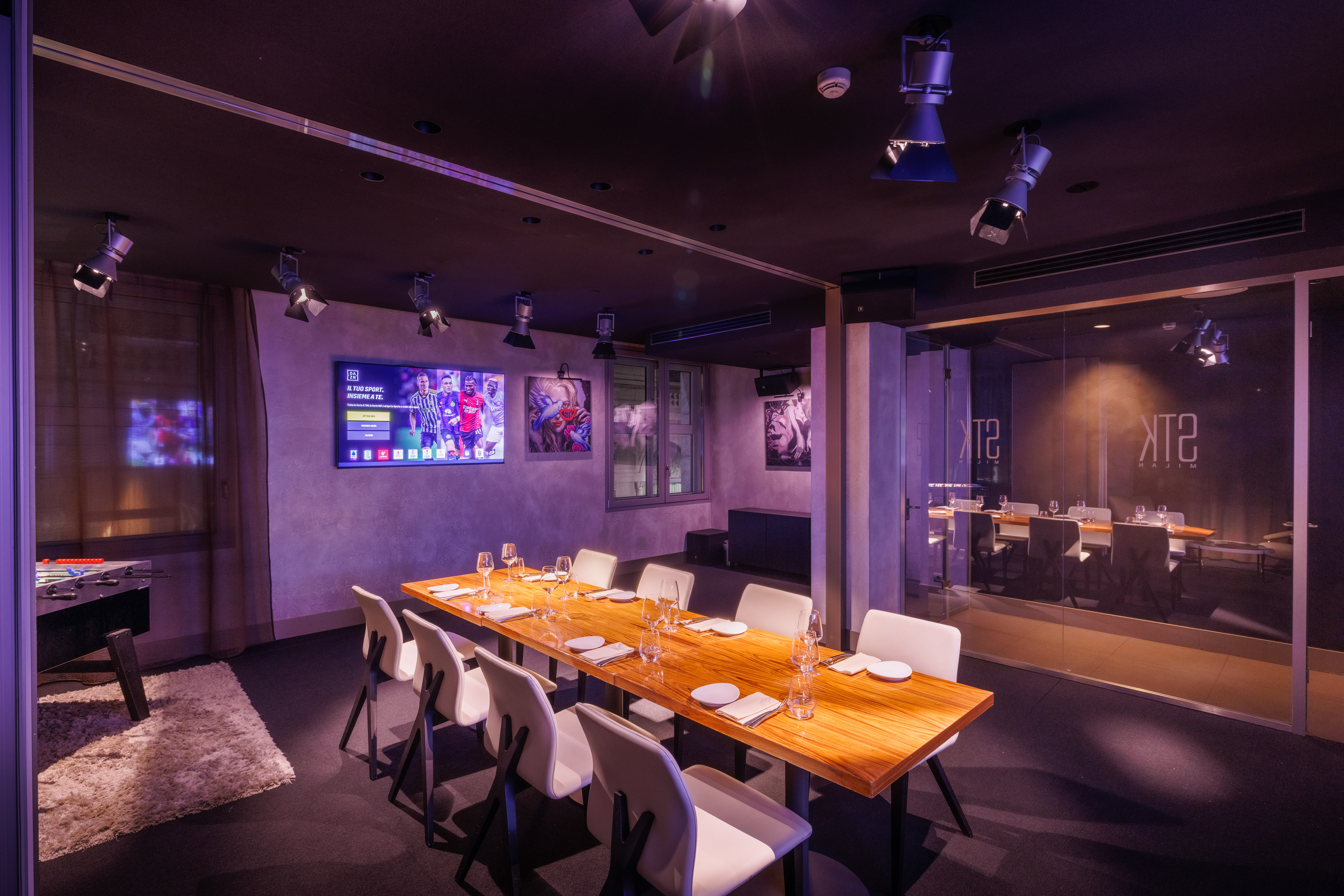 Private sports lounge with long dining table, TV, foosball, and modern decor.