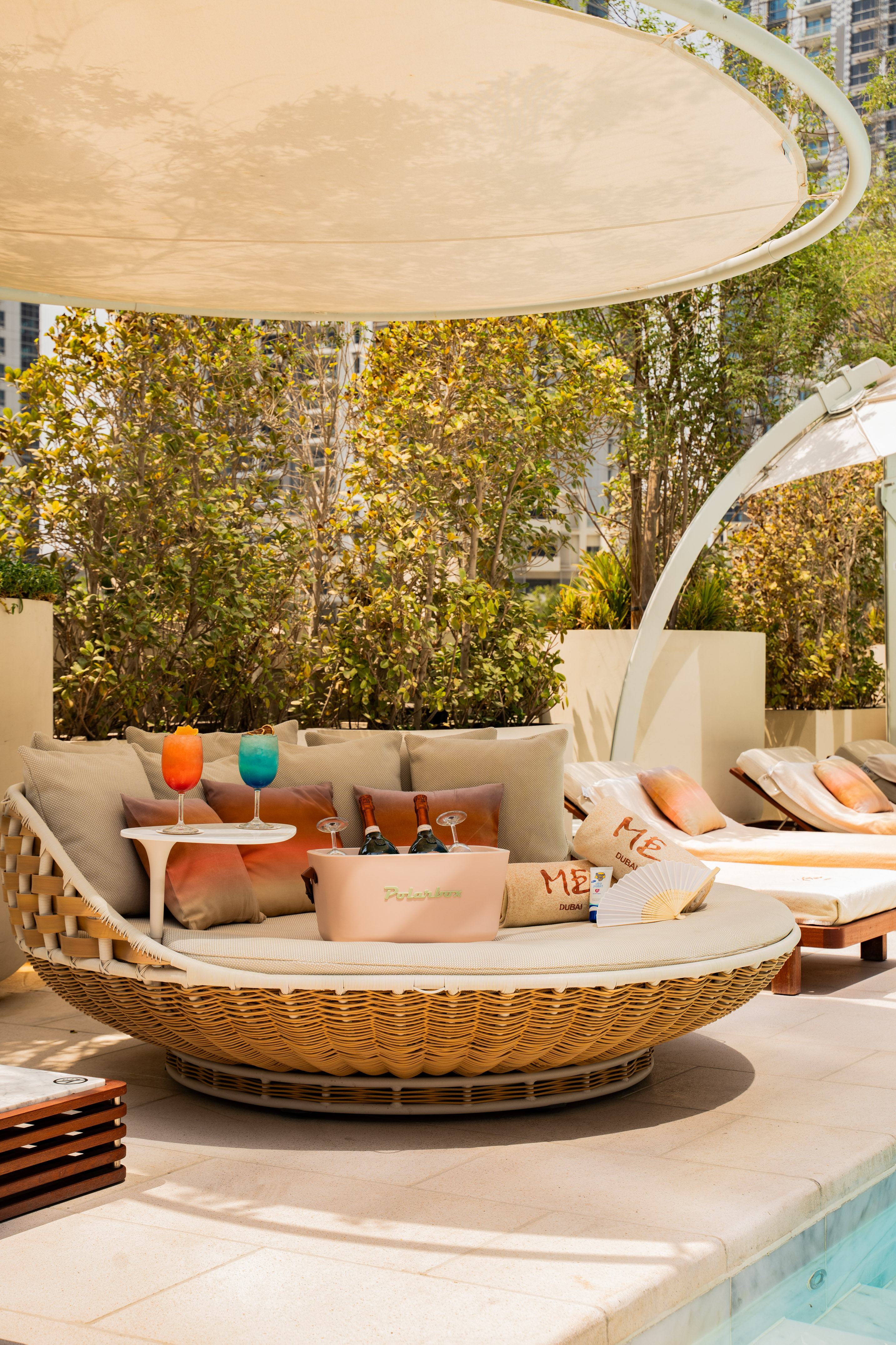Luxurious poolside daybed with colorful cocktails, champagne, and ME Dubai essentials.