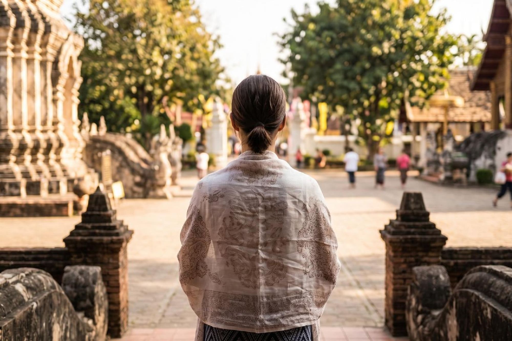 Woman in shawl observing ornate Thai temple architecture.