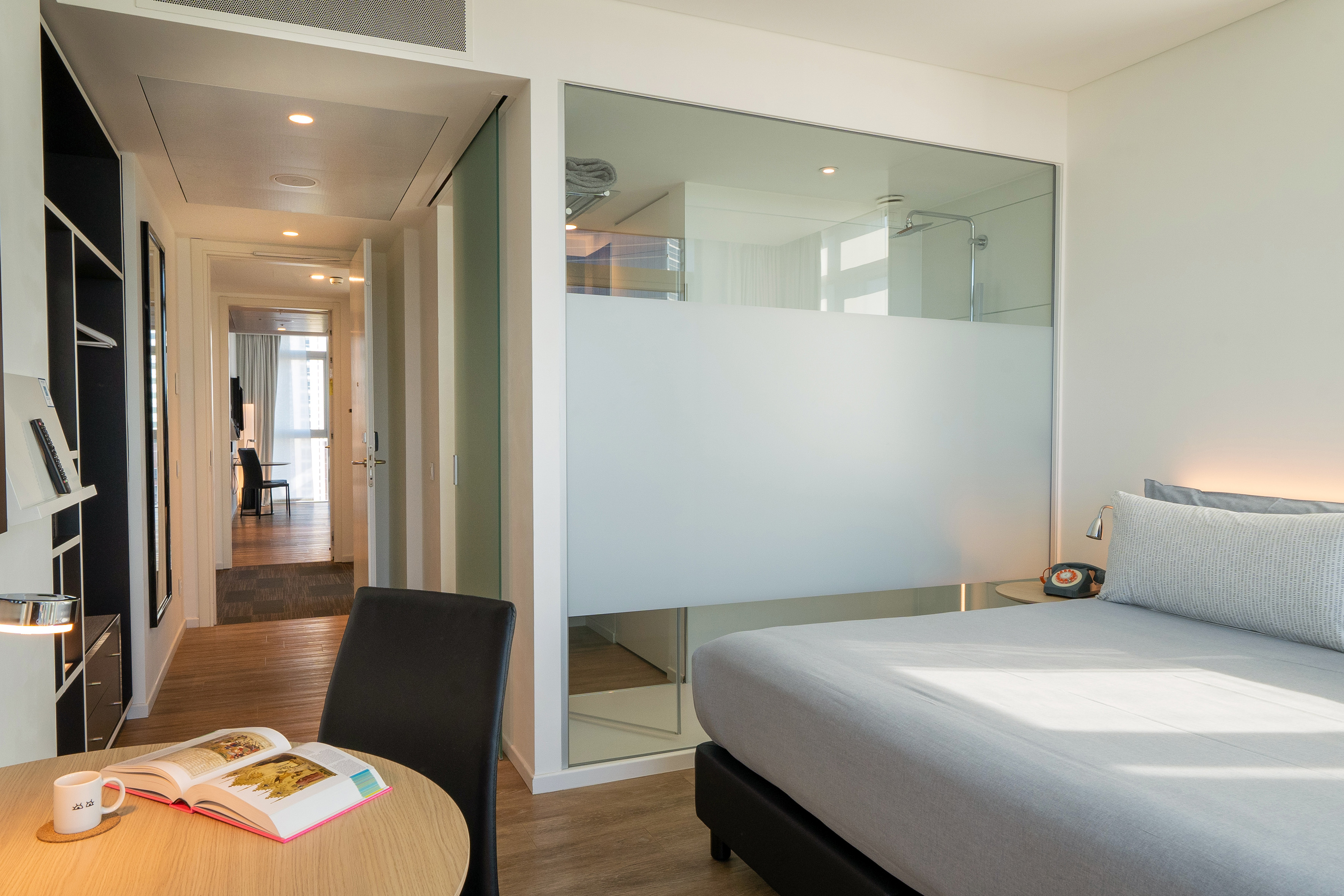 Modern hotel room with bed, frosted glass shower, and work desk.