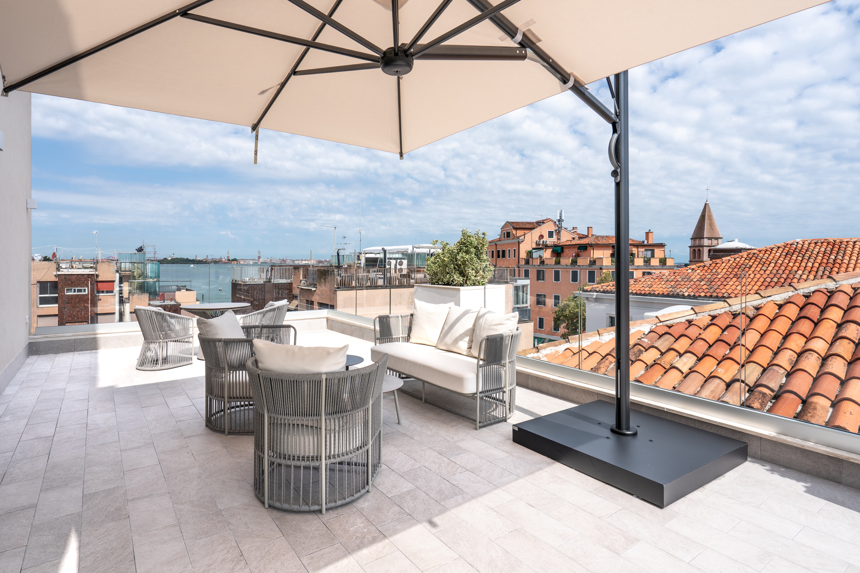 Rooftop terrace with modern outdoor furniture, umbrella, and Venice city view.