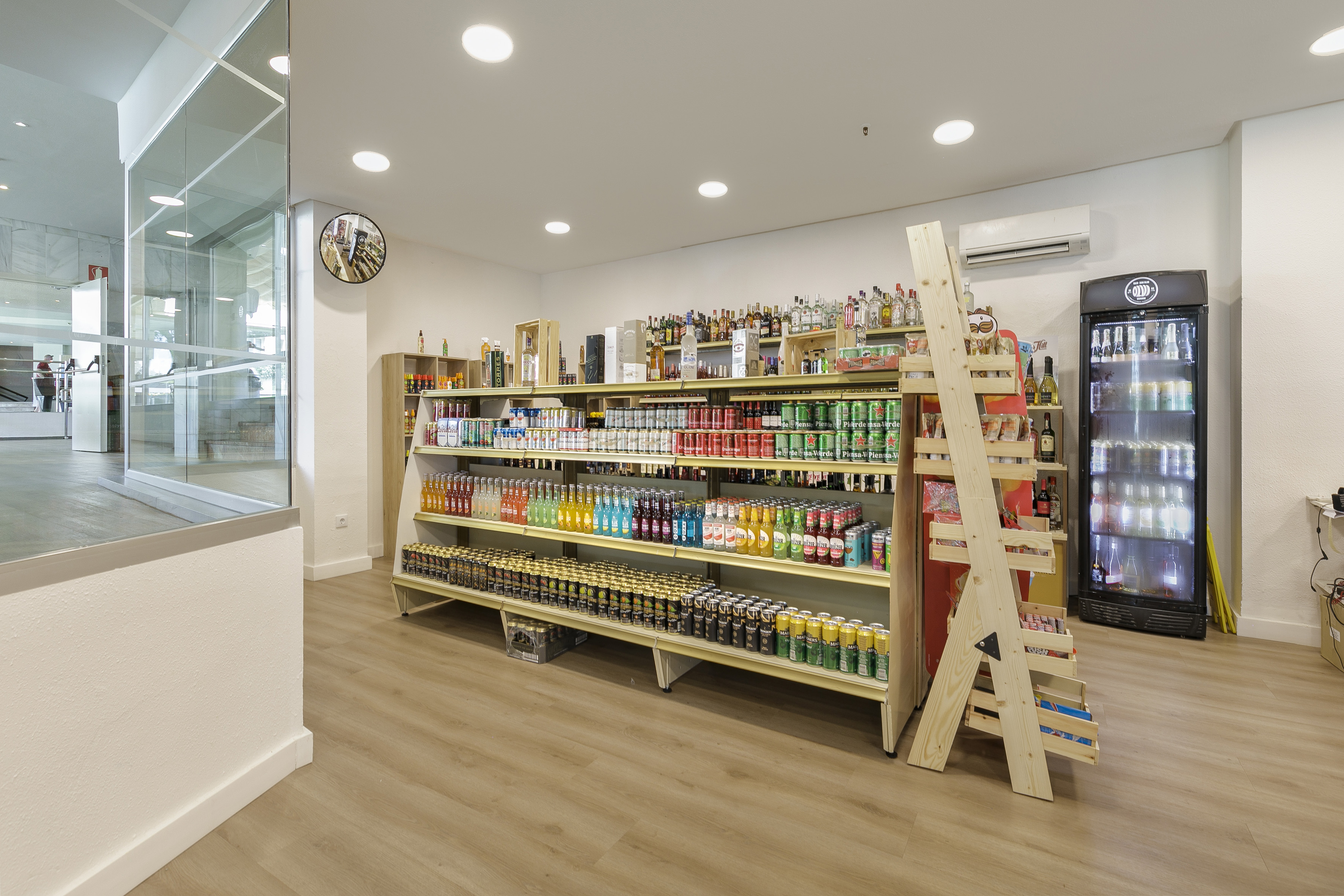 Bright minimart with shelves of sodas, spirits, and a large drink cooler.