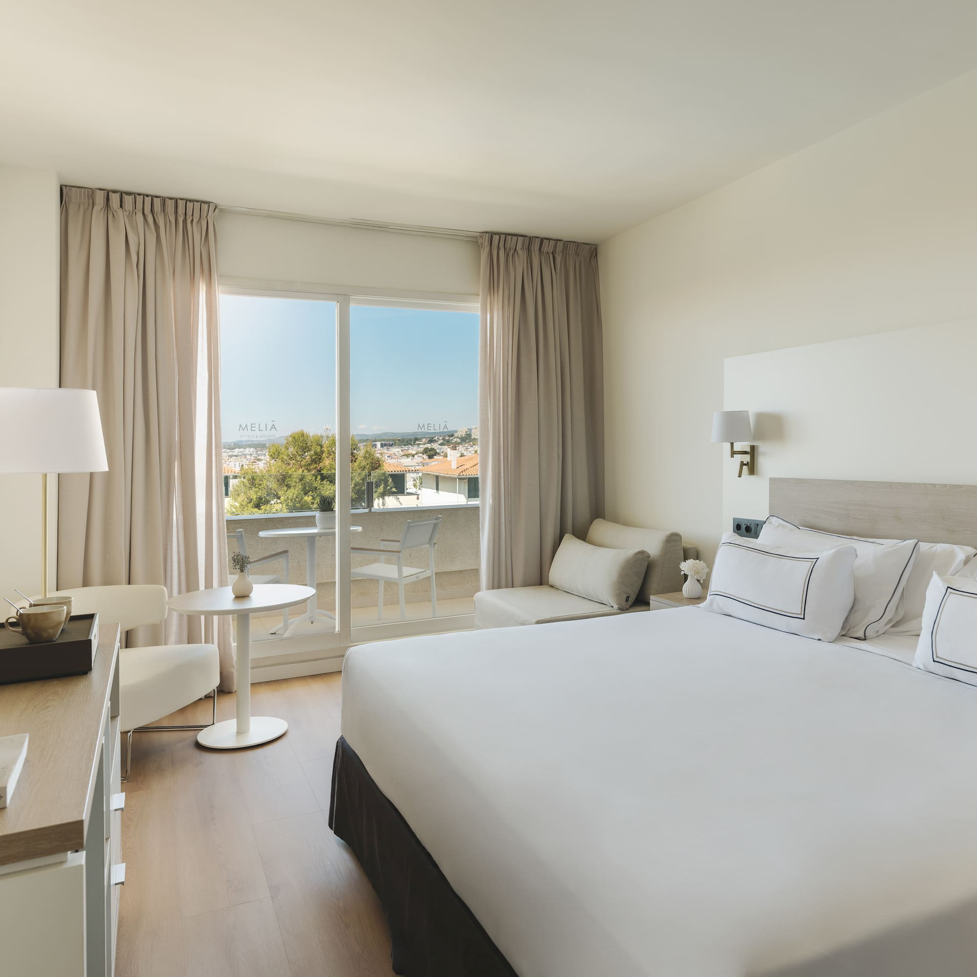 Luminosa habitación hotel Meliá con balcón, cama doble y vistas a la ciudad.
