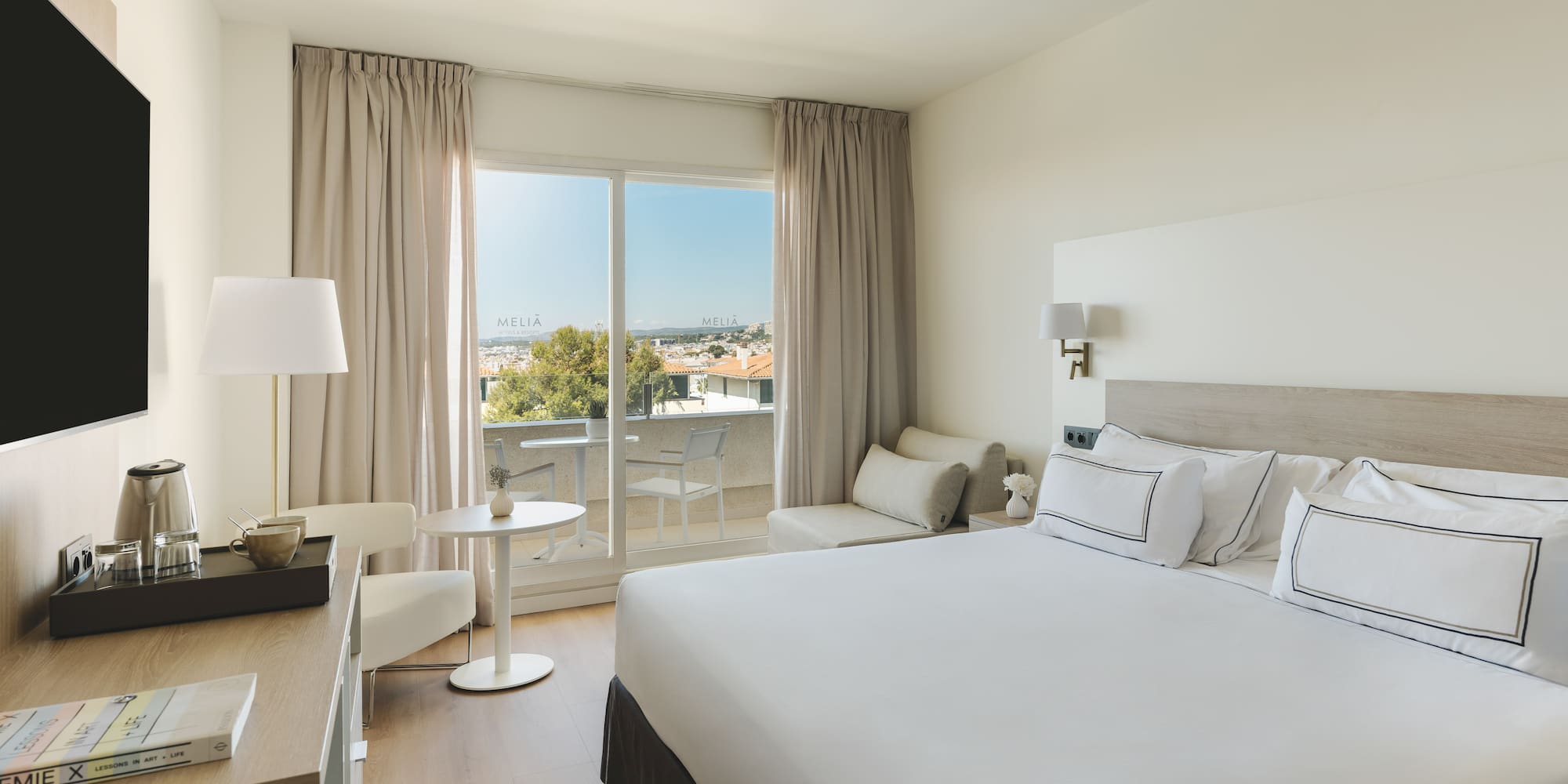 Luminosa habitación hotel Meliá con balcón, cama doble y vistas a la ciudad.