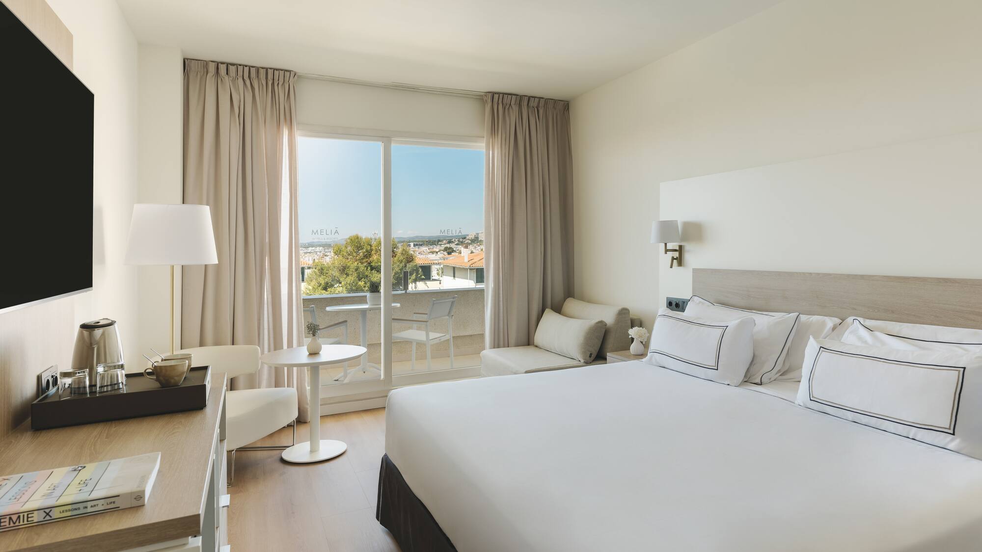 Luminosa habitación hotel Meliá con balcón, cama doble y vistas a la ciudad.