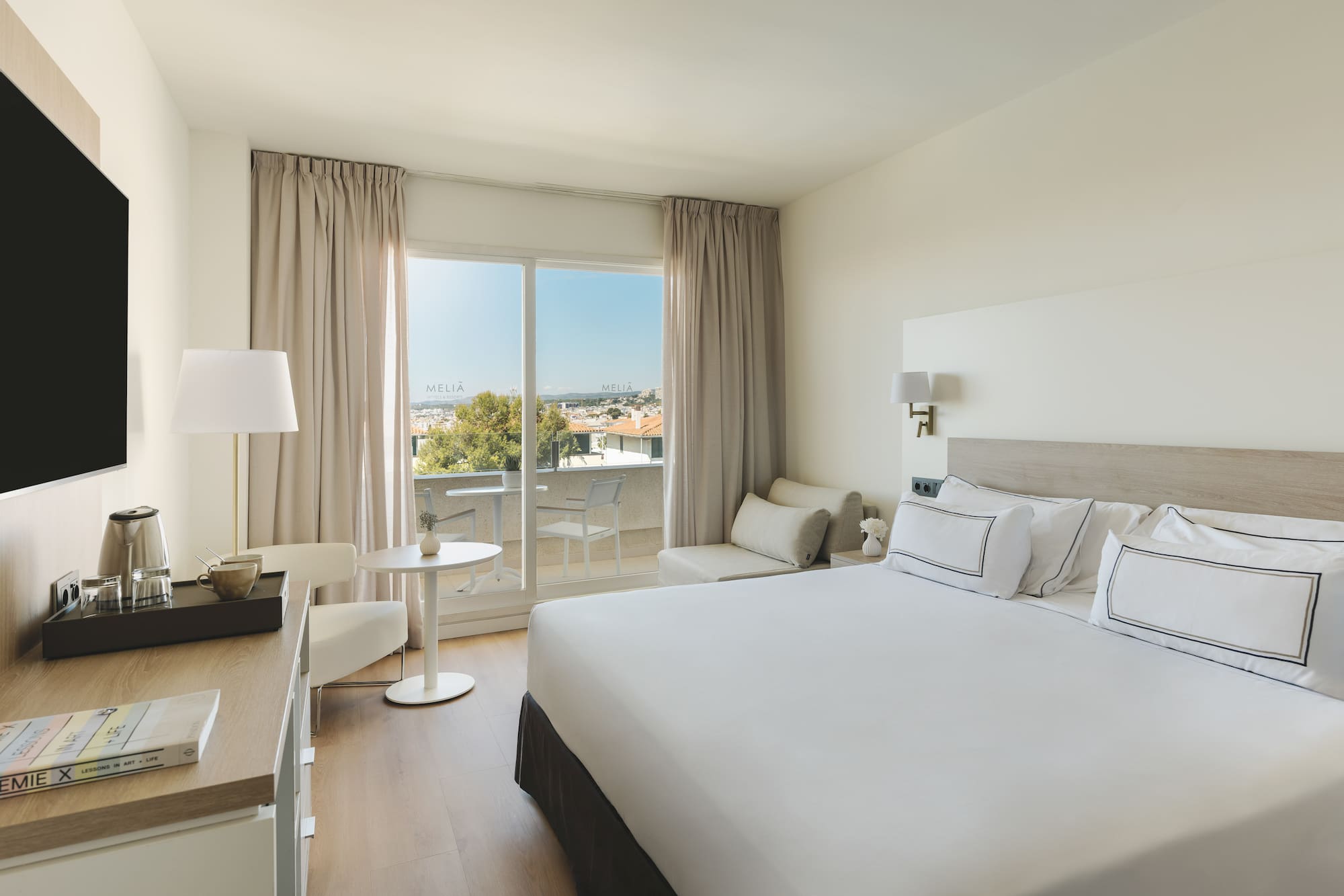 Luminosa habitación hotel Meliá con balcón, cama doble y vistas a la ciudad.