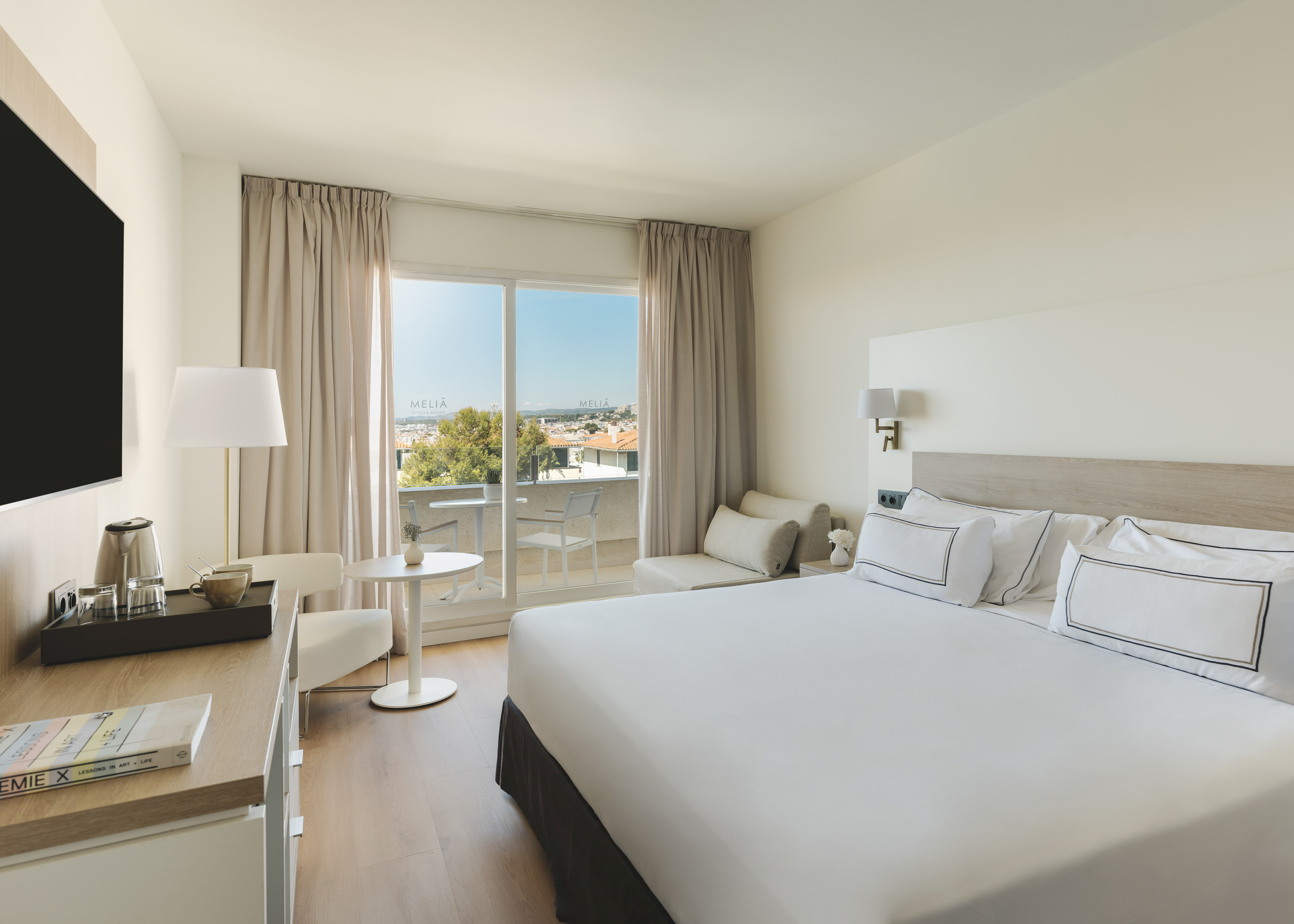 Luminosa habitación hotel Meliá con balcón, cama doble y vistas a la ciudad.