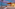 Illuminated beachfront restaurant with outdoor seating, sandy beach, and twilight sky.