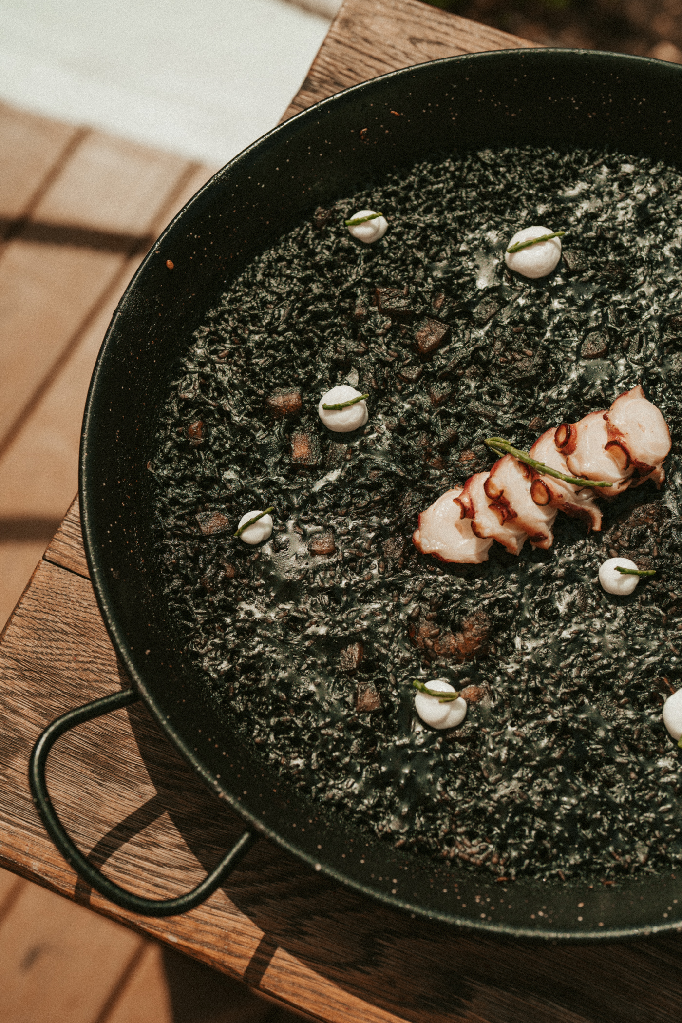 Squid ink paella (arroz negro) with octopus and aioli on a wooden table.