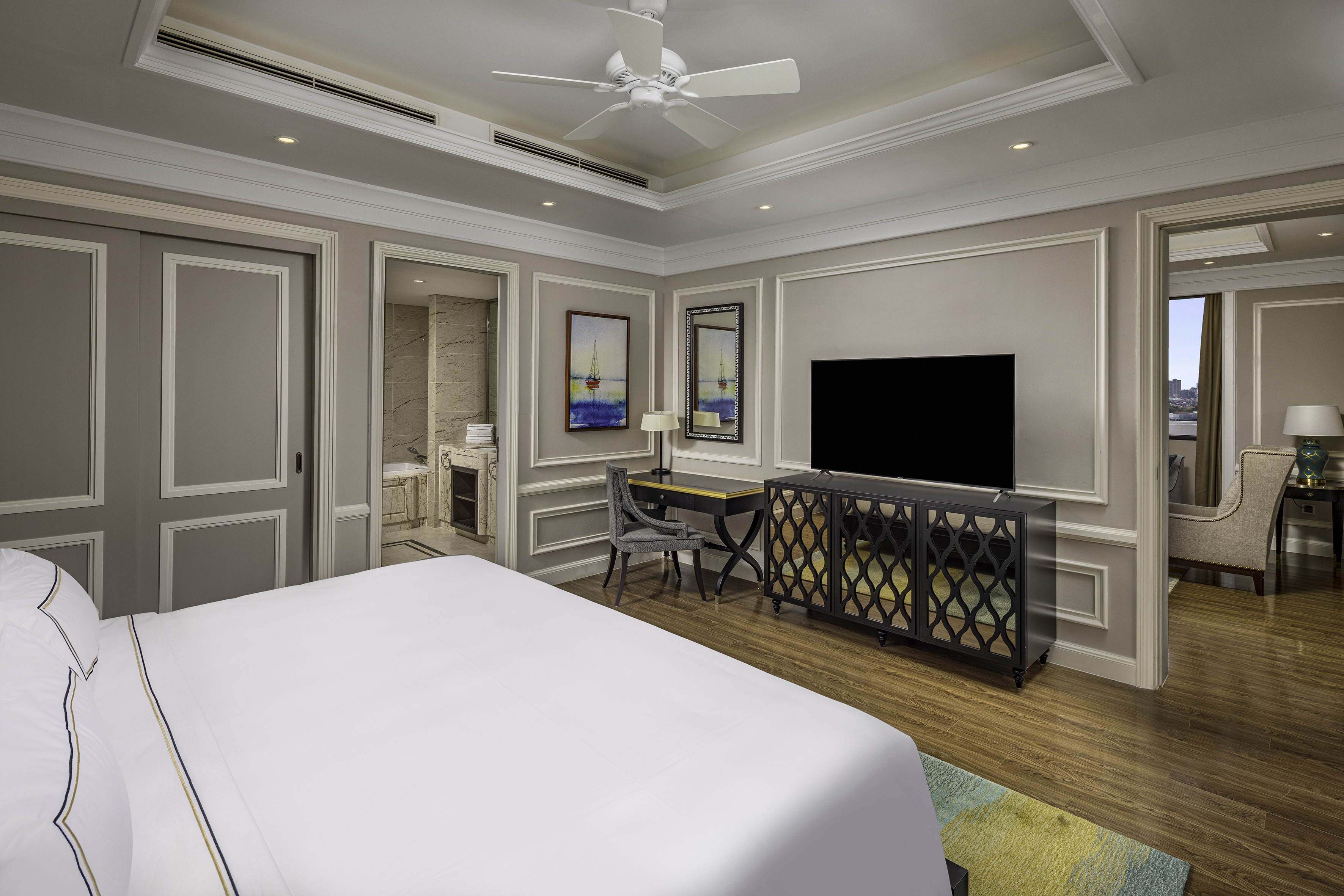 Luxury hotel room: white bed, TV, desk, wood floor, adjoining bathroom.