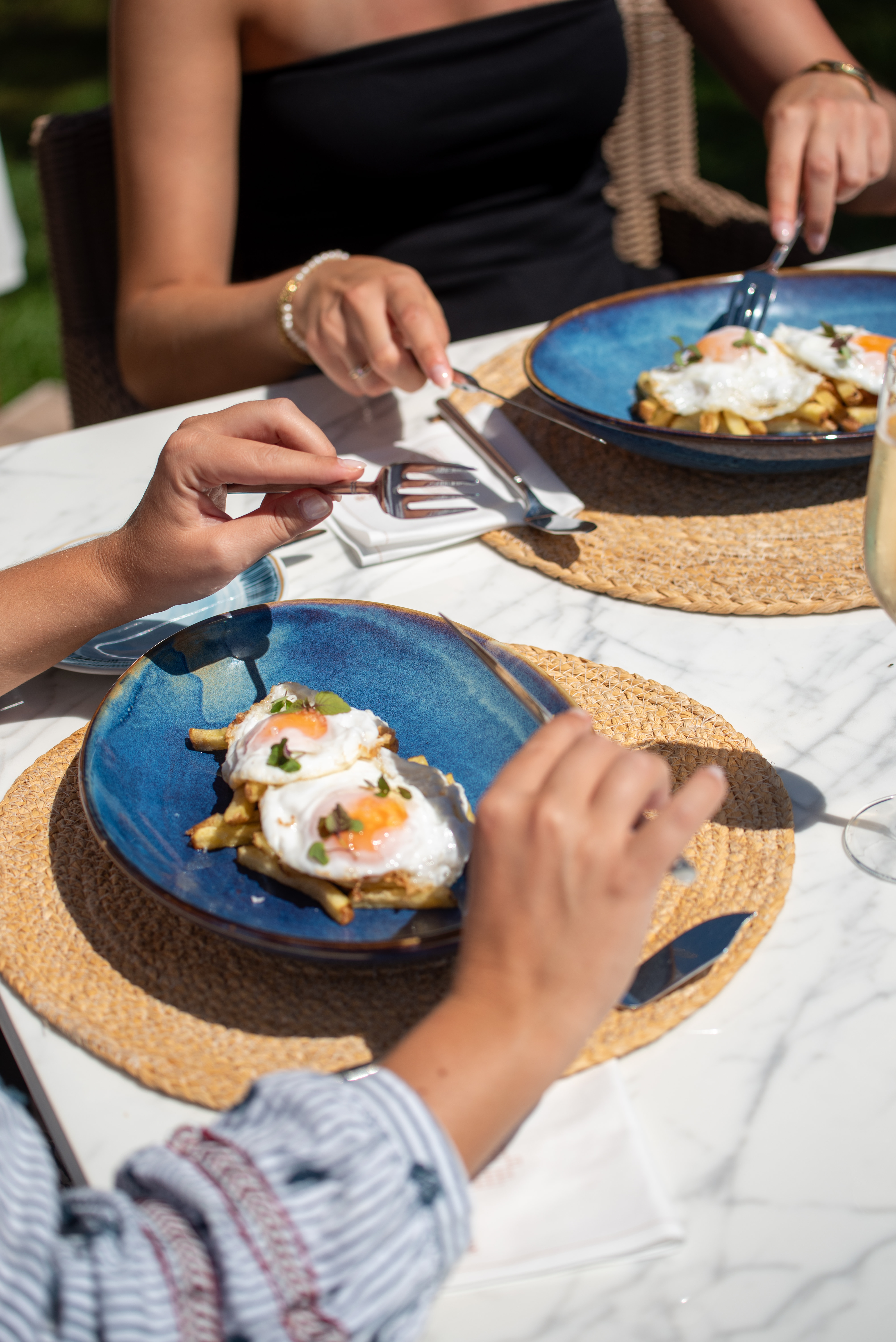 Two people eating fried eggs and fries on blue plates at an outdoor brunch.