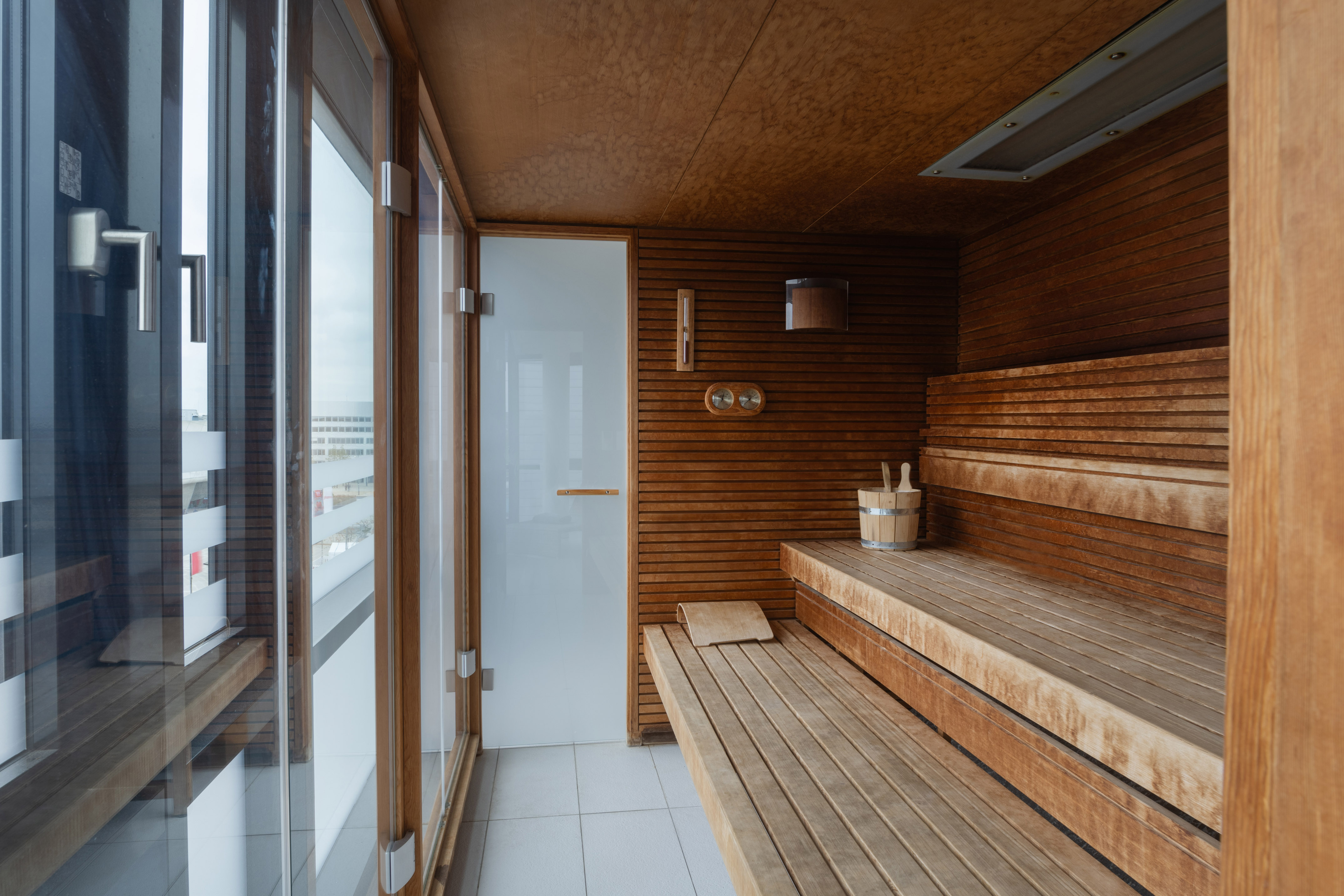 Modern wood sauna interior with tiered benches and large glass window. - Phòng xông hơi với tầm nhìn công nghiệp - INNSiDE Wolfsburg, Wolfsburg