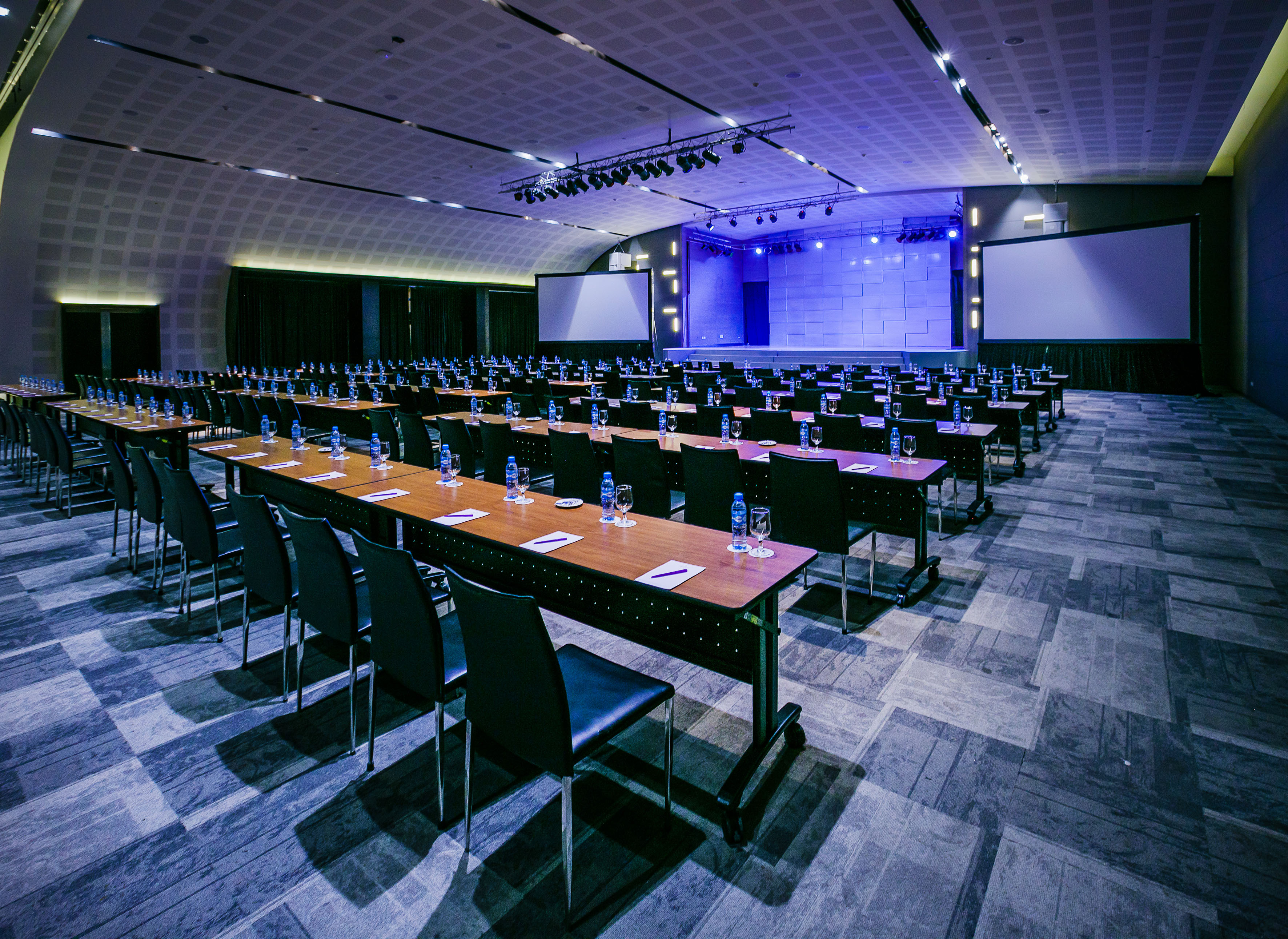 Modern conference room setup with tables, chairs, stage, and projection screens.