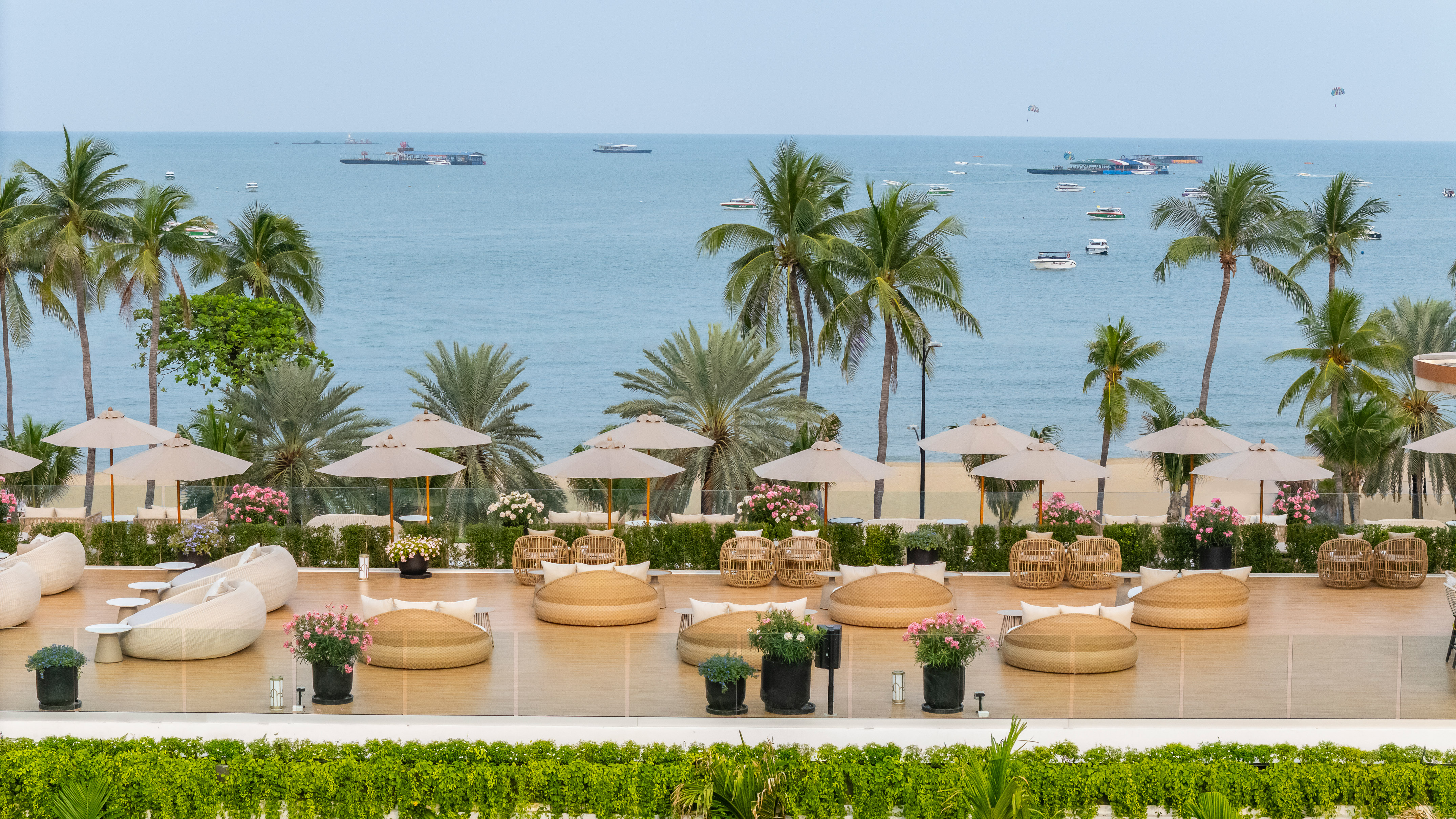 Beach resort terrace with lounge seating, palm trees, and ocean view.