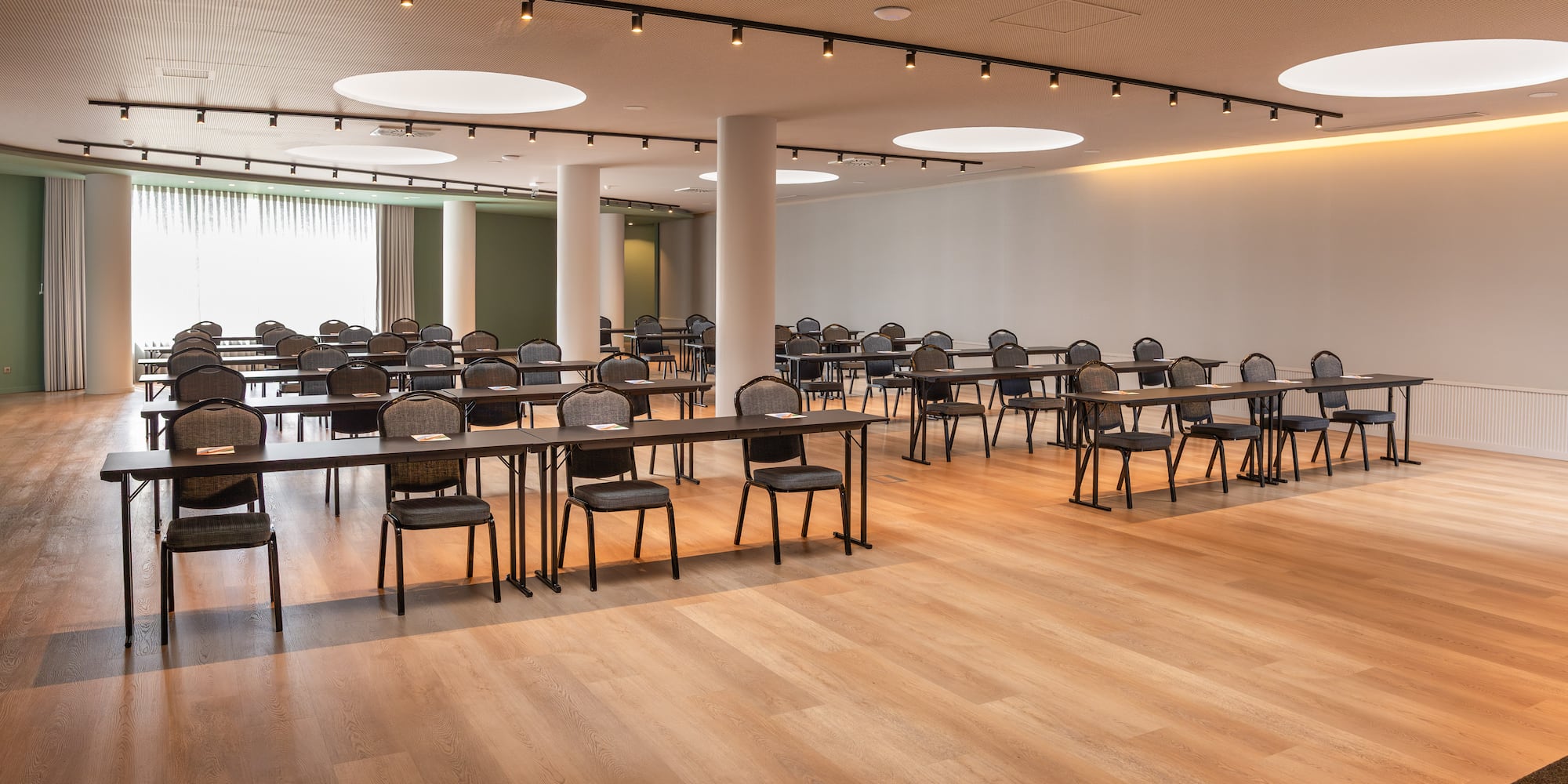 Empty modern conference room with rows of tables and chairs, wood flooring.