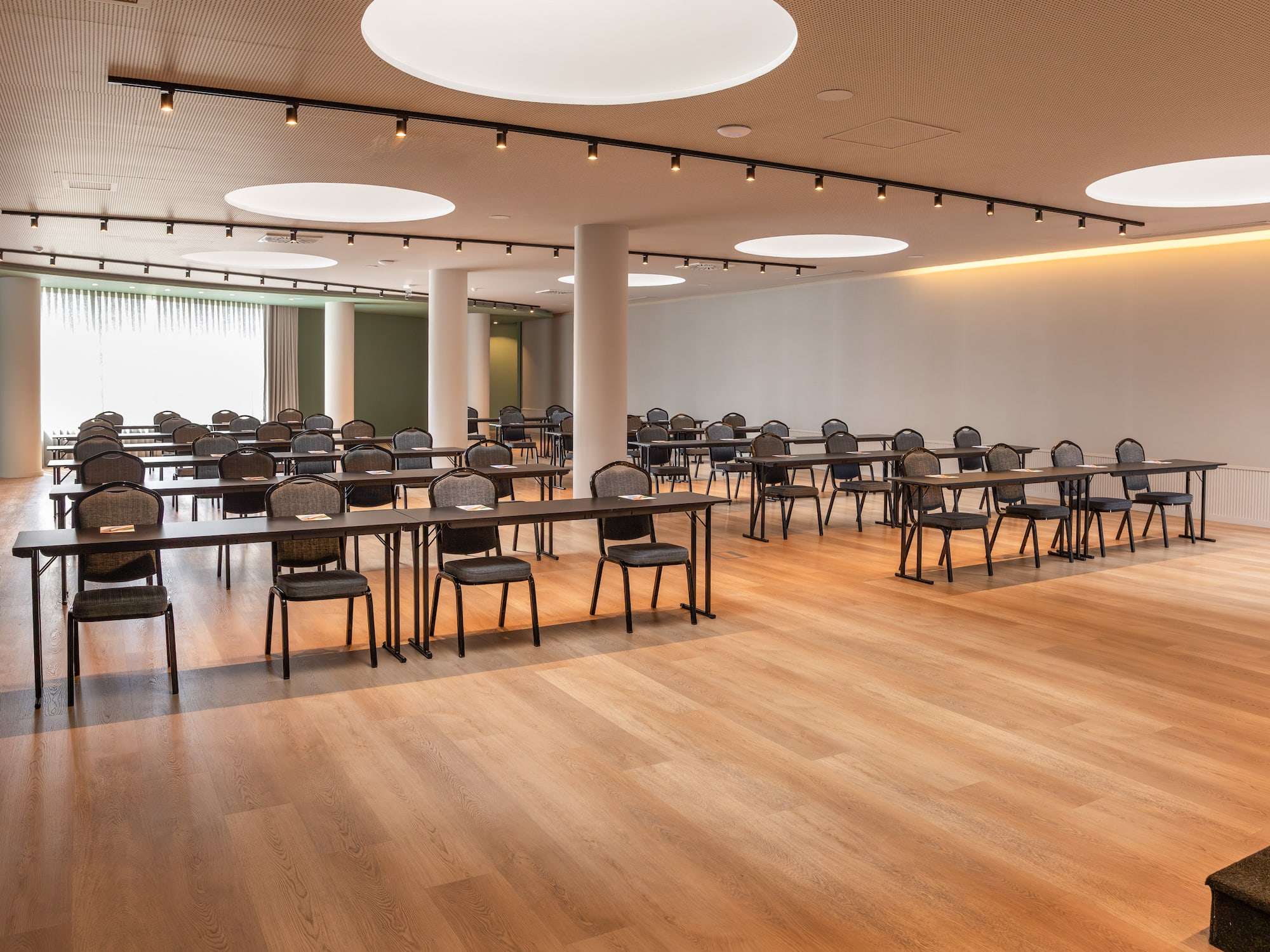 Modern conference room with tables and chairs, wooden floor, ample light.