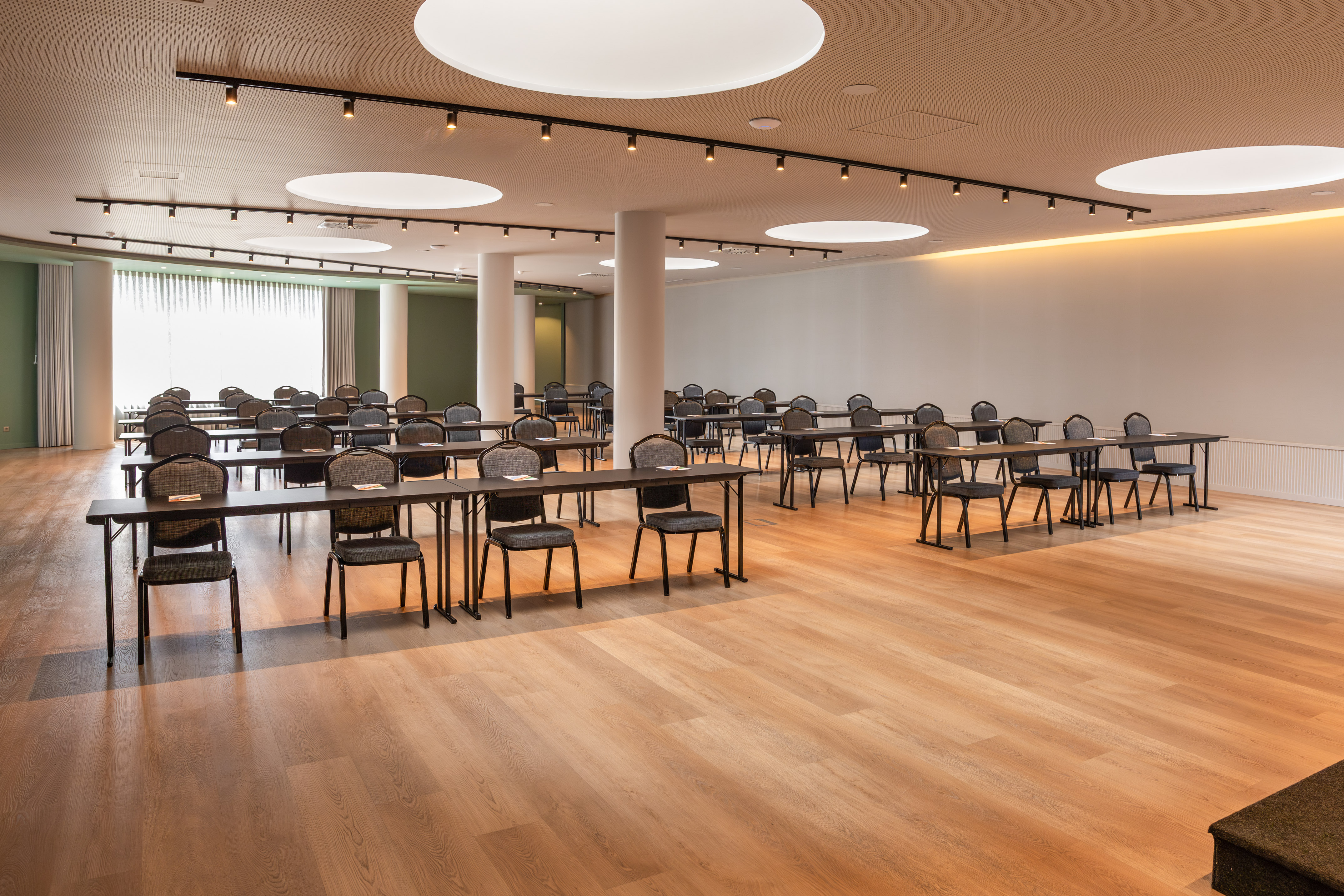Empty modern conference room with rows of tables and chairs, wood flooring.
