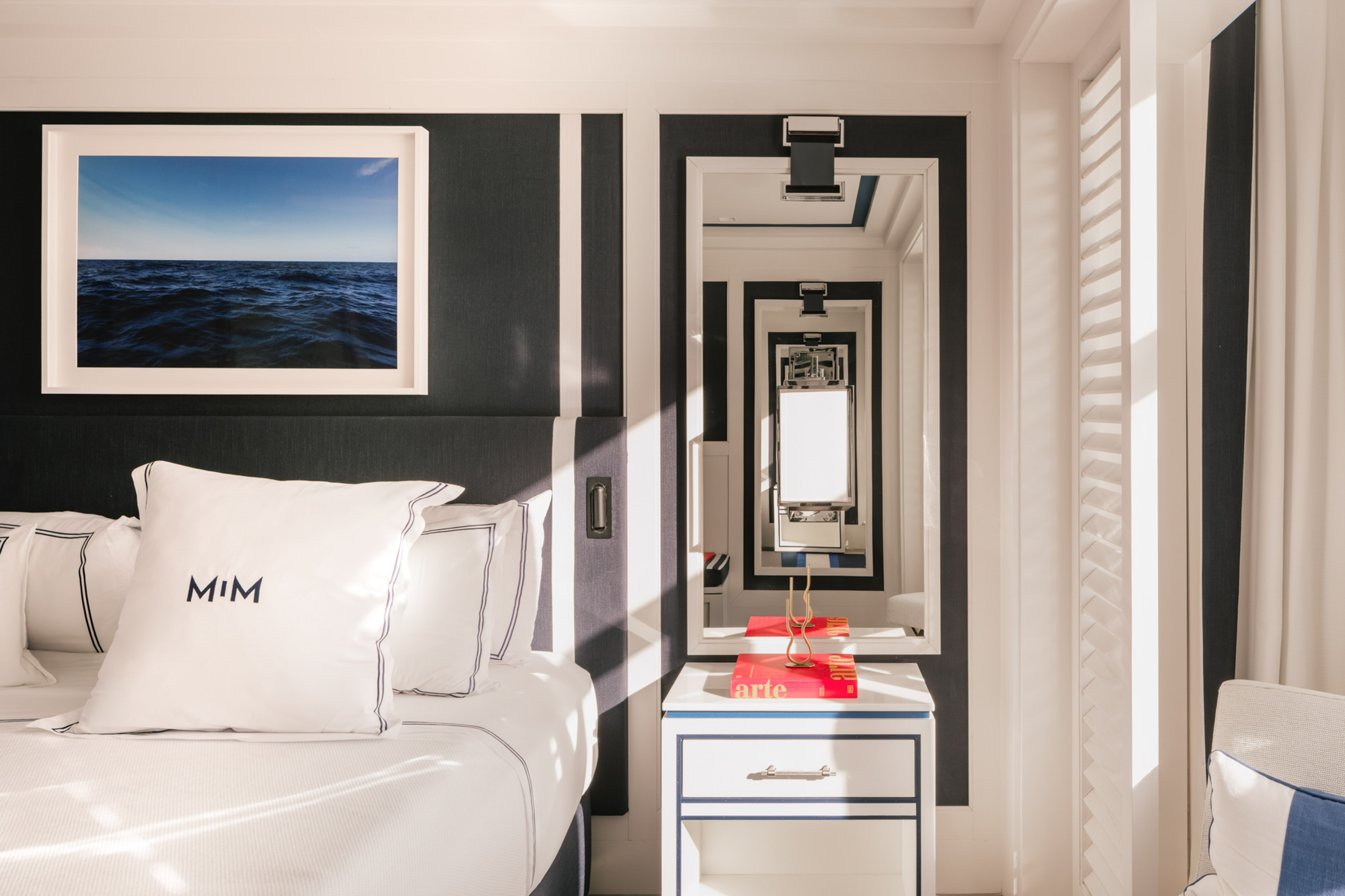 Luxury hotel bedroom with nautical striped wall, seascape art, white bedding.