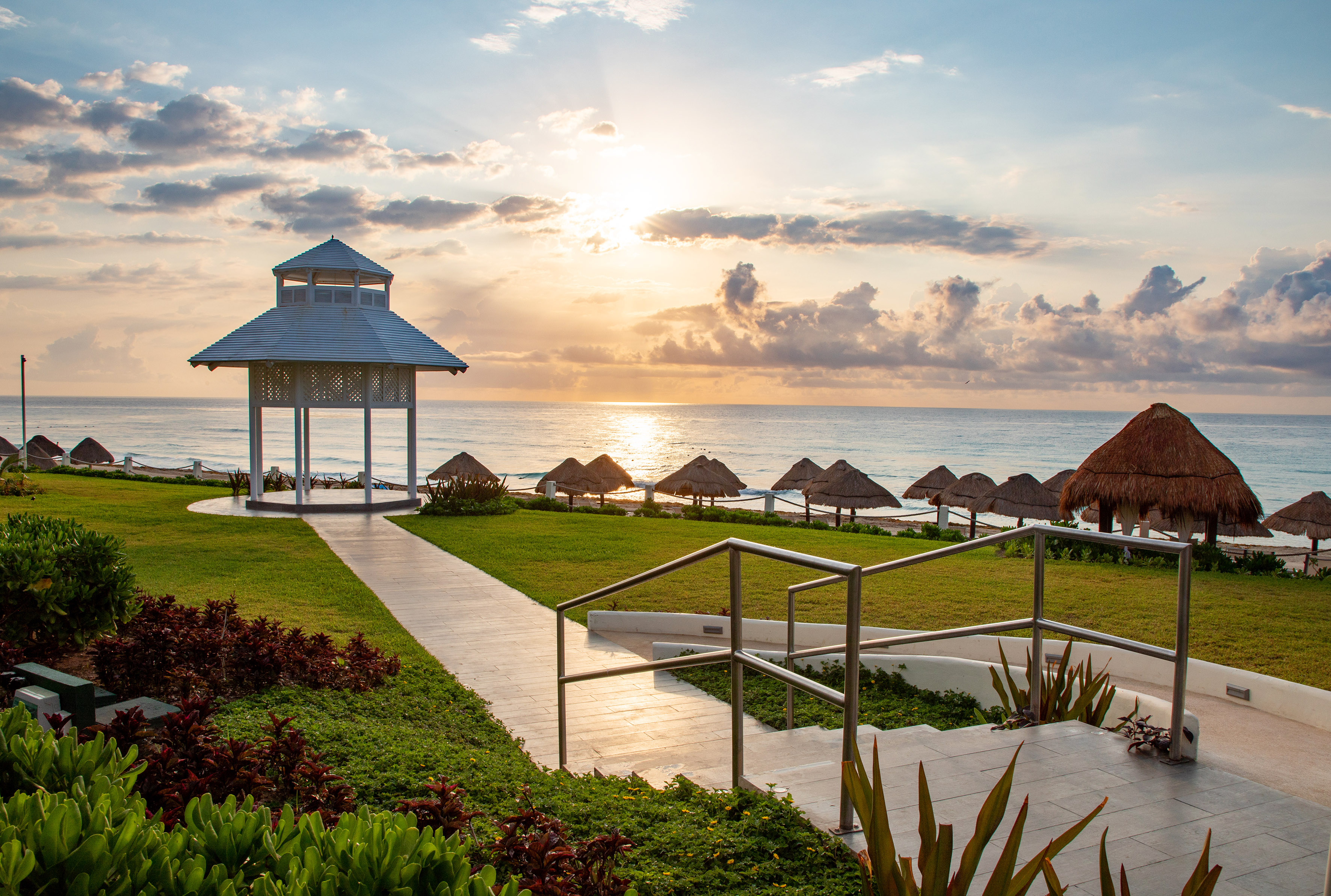 Coastal resort sunrise with a white gazebo, ocean, and beach palapas.