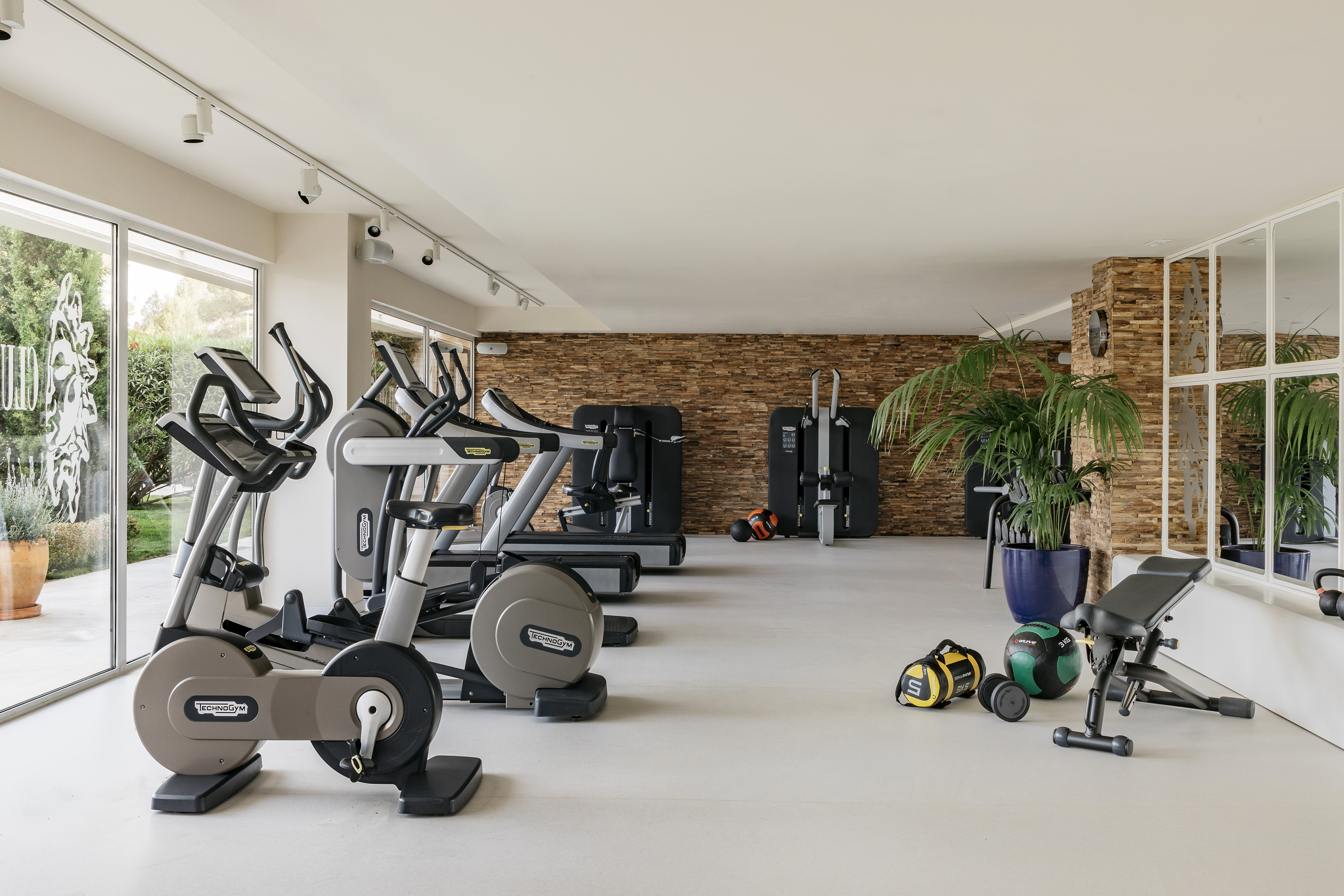 Modern gym with Technogym cardio equipment, free weights, and stone feature wall.