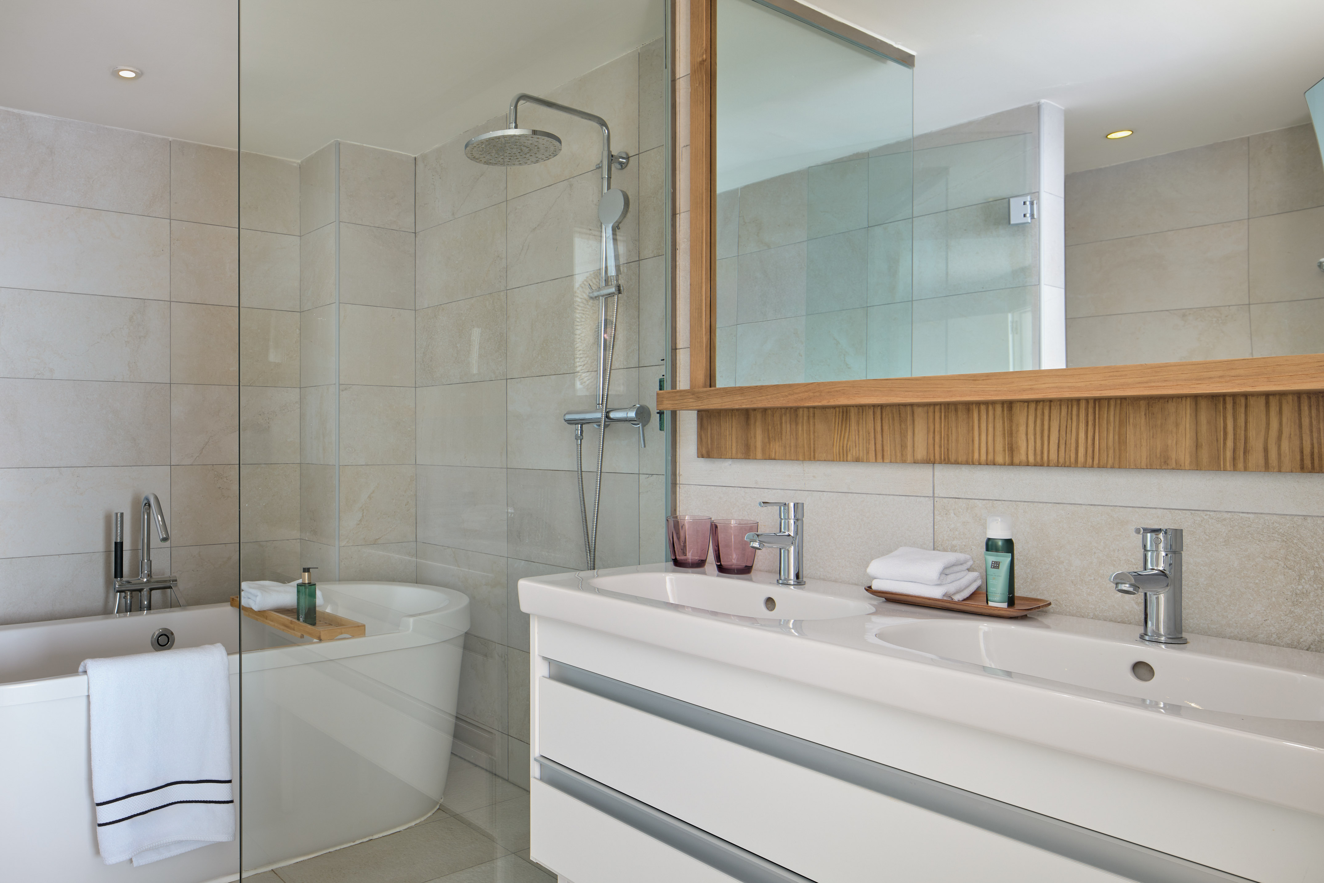 Modern tiled bathroom with bathtub, glass shower, and double vanity.