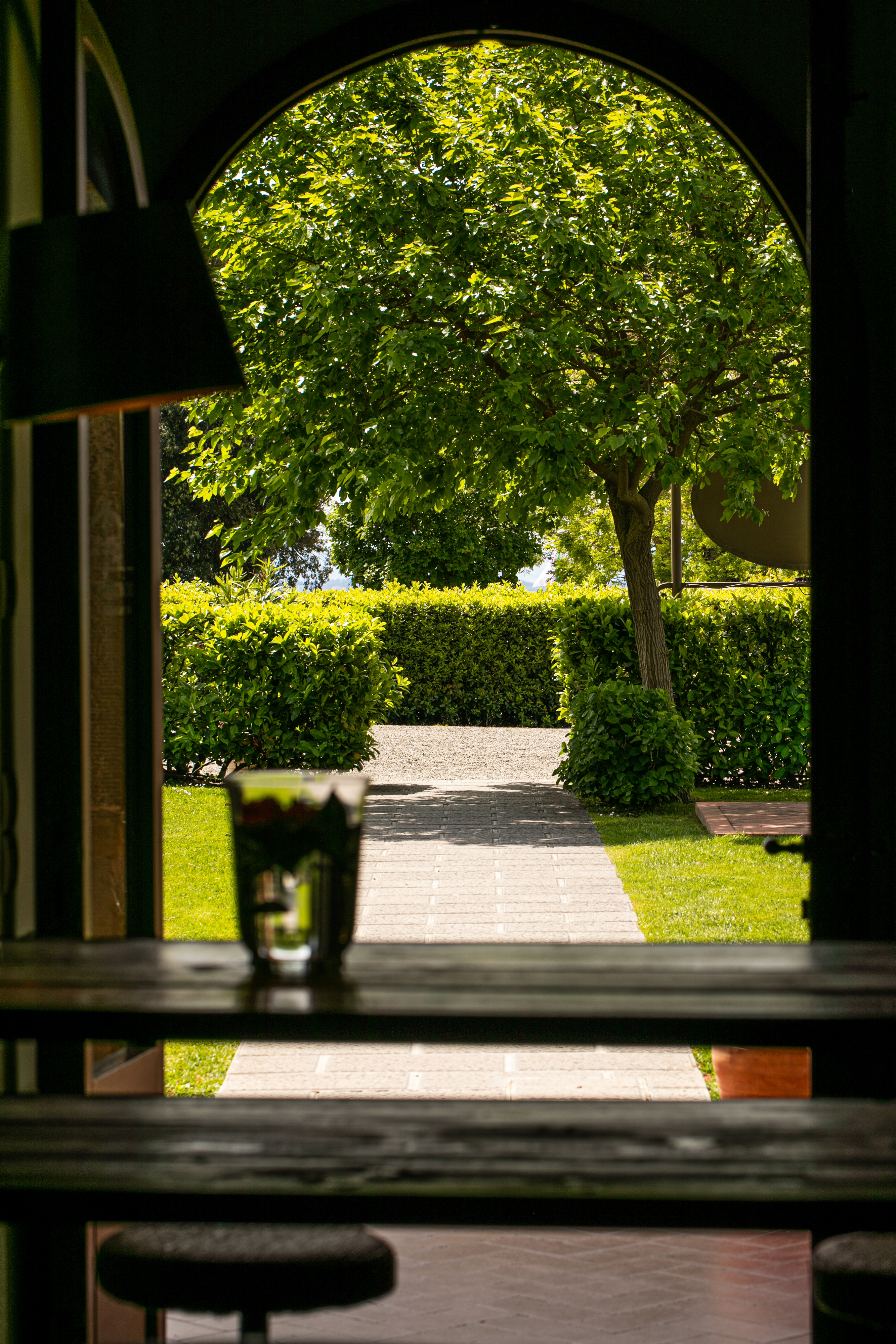Archway framing a sunny garden path, lush trees, and green hedges.
