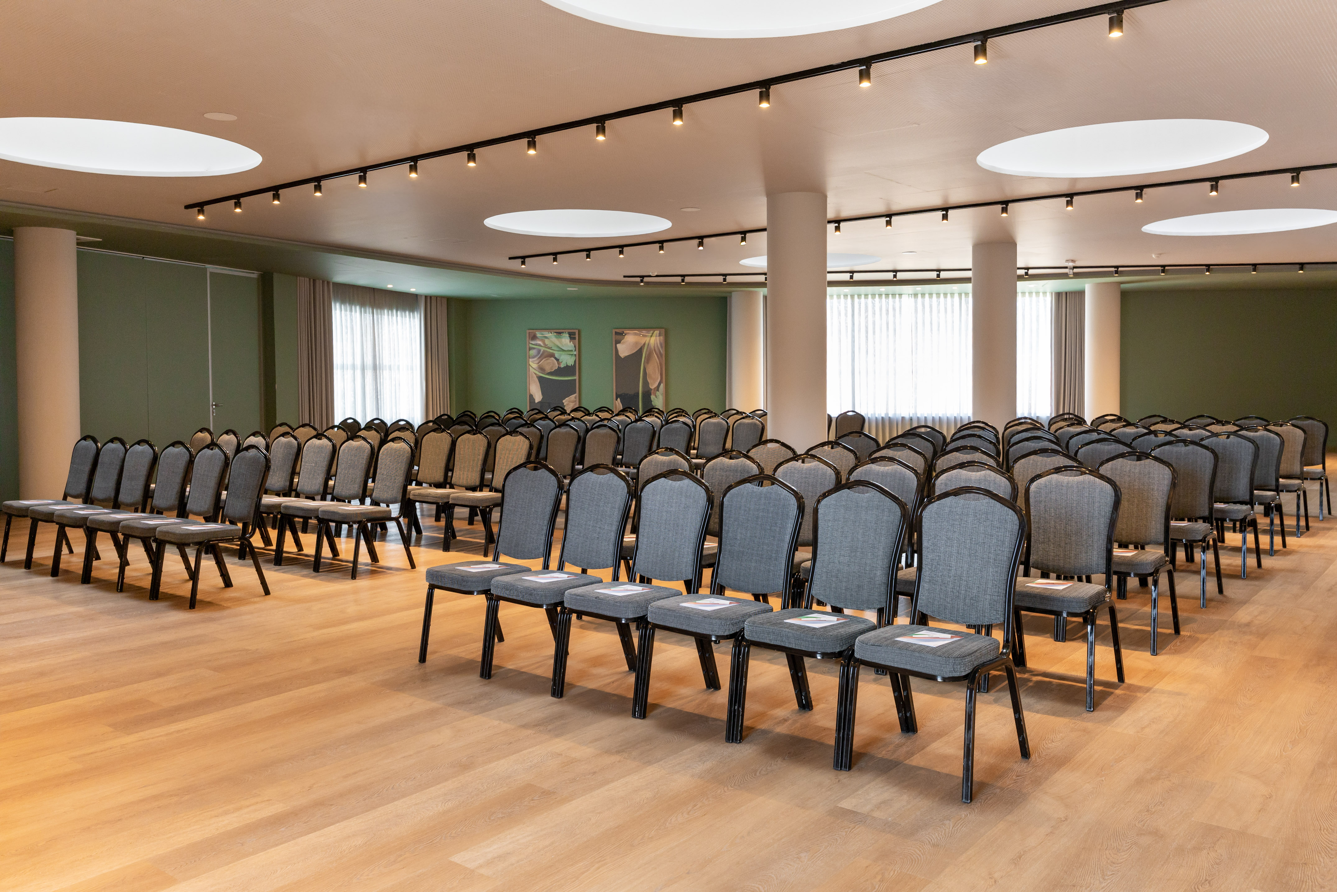 Spacious empty conference room with rows of grey chairs, hardwood floor, and green walls.