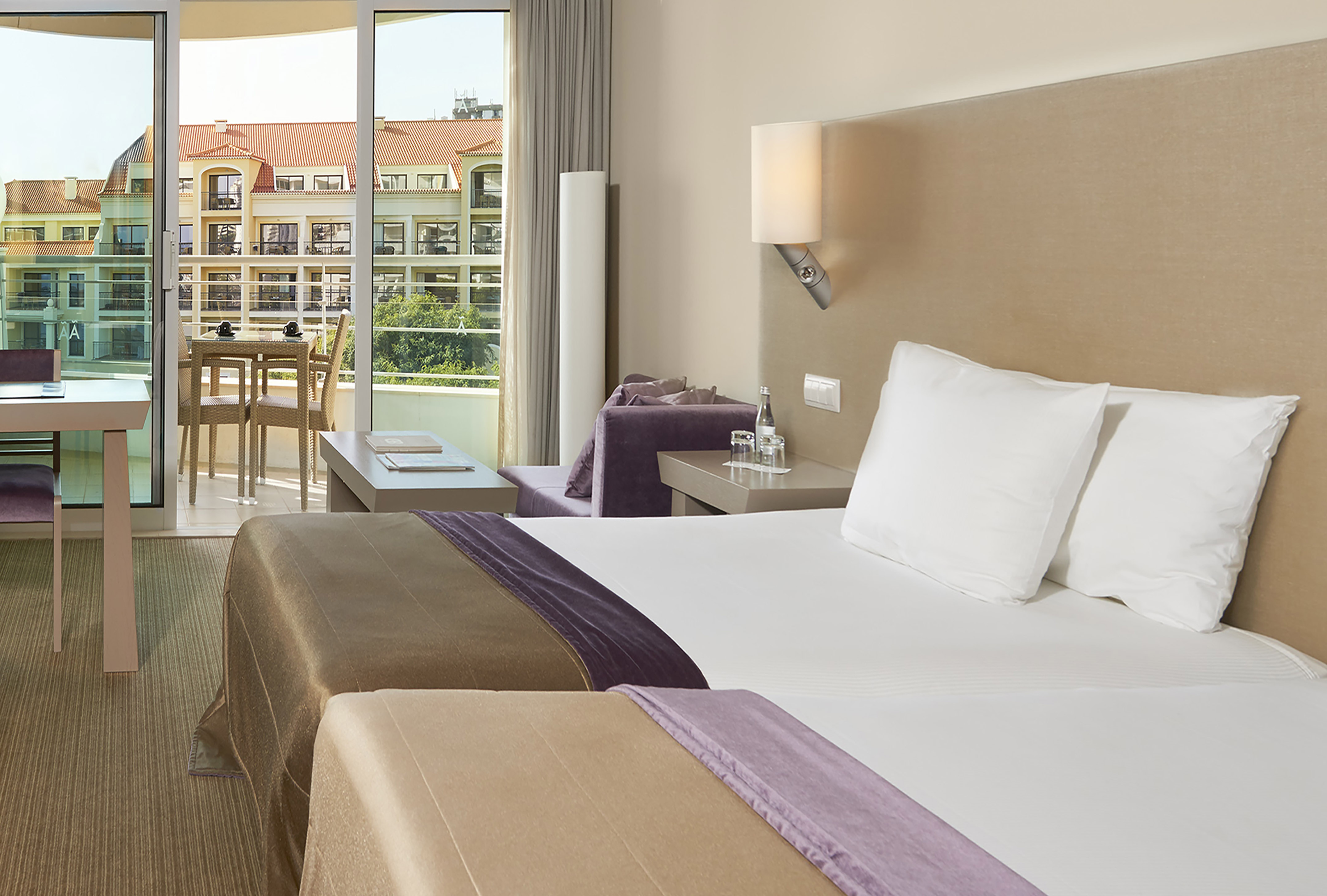 Modern hotel room with bed, sofa, private balcony, and resort view.