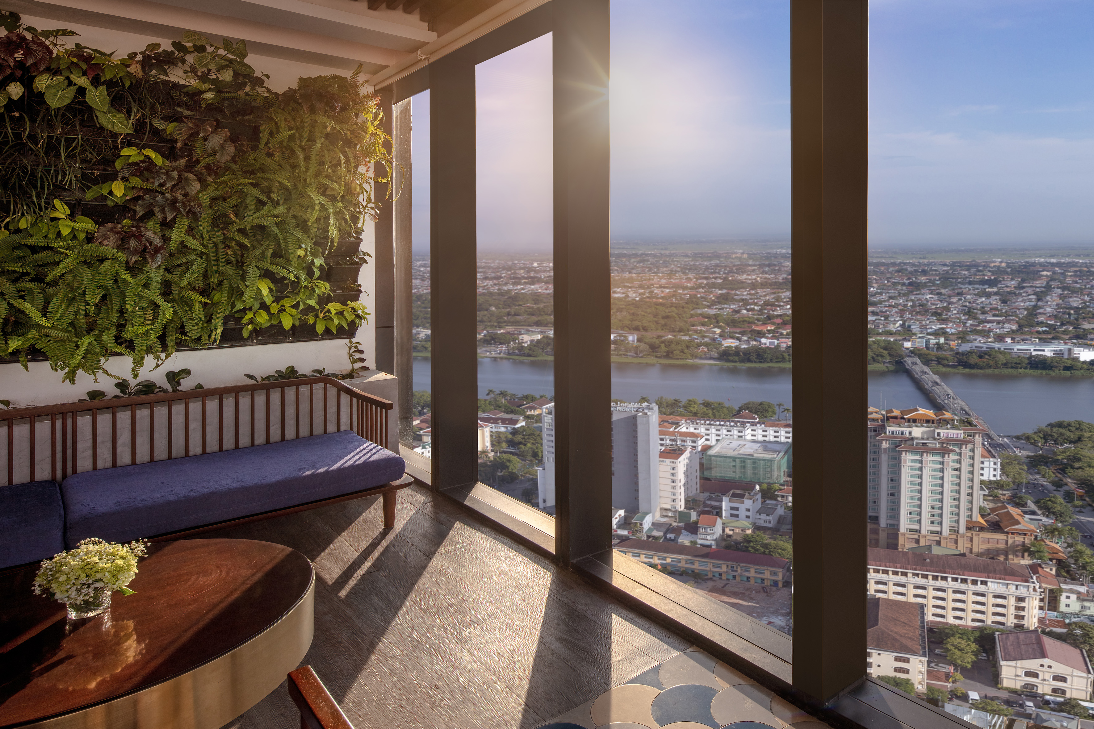 Balcony lounge with green wall, sofa, and sunny city river and bridge view.