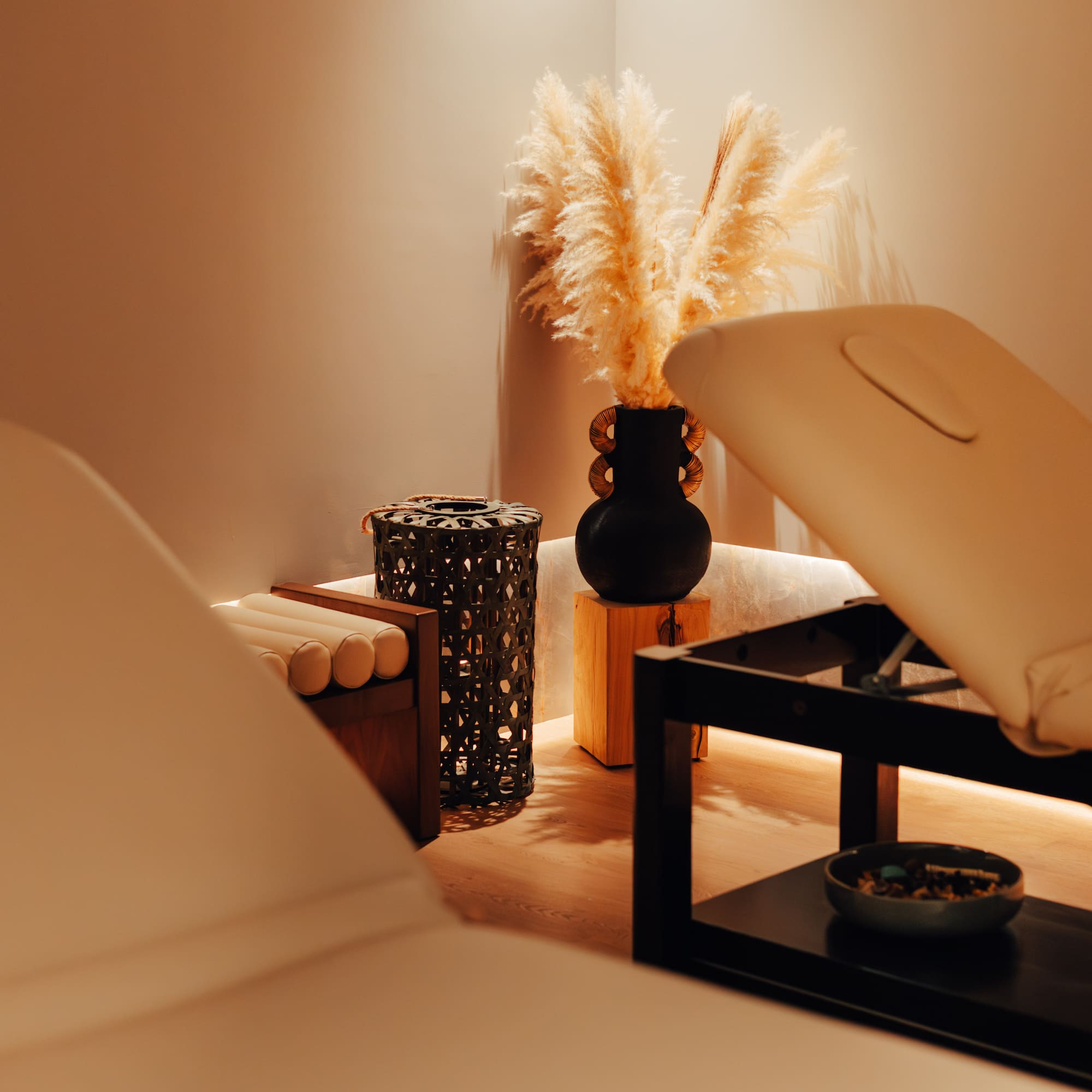 Warmly lit spa room with two massage beds and decorative pampas grass.