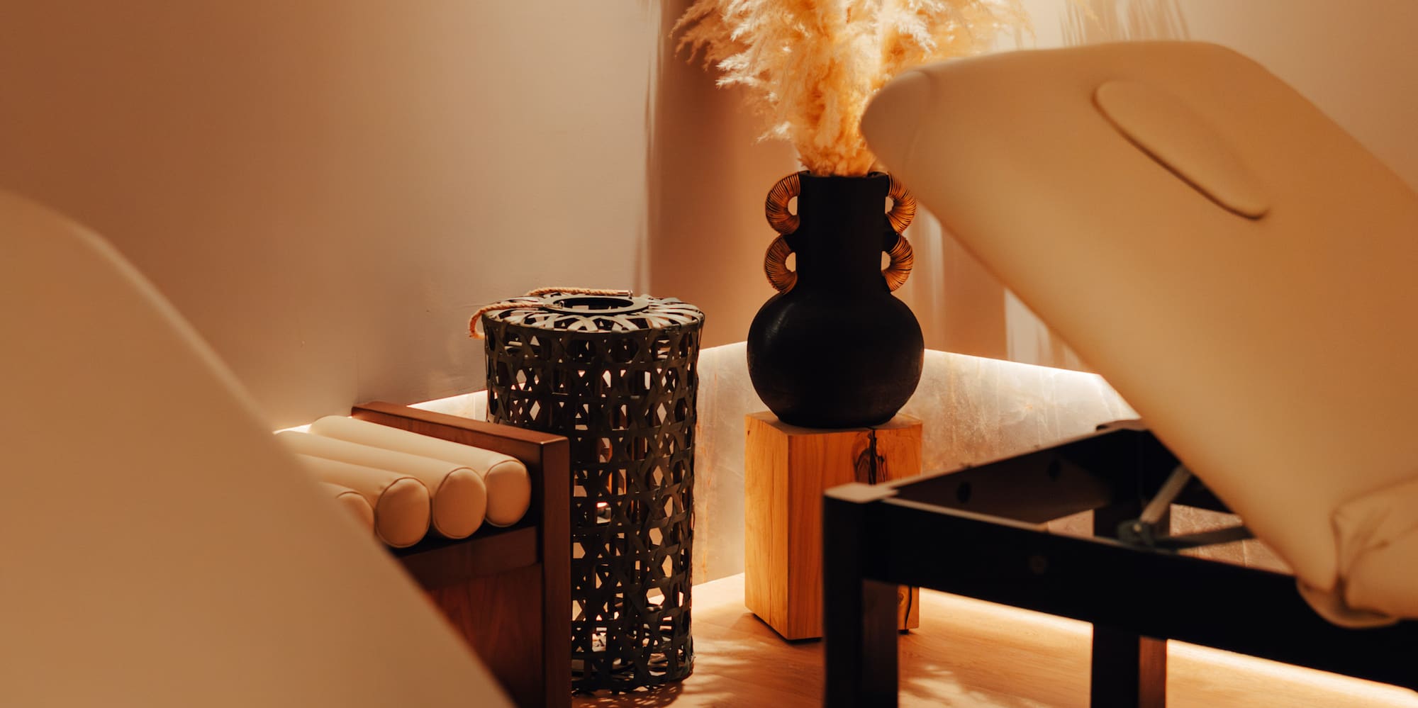 Warmly lit spa room with two massage beds and decorative pampas grass.