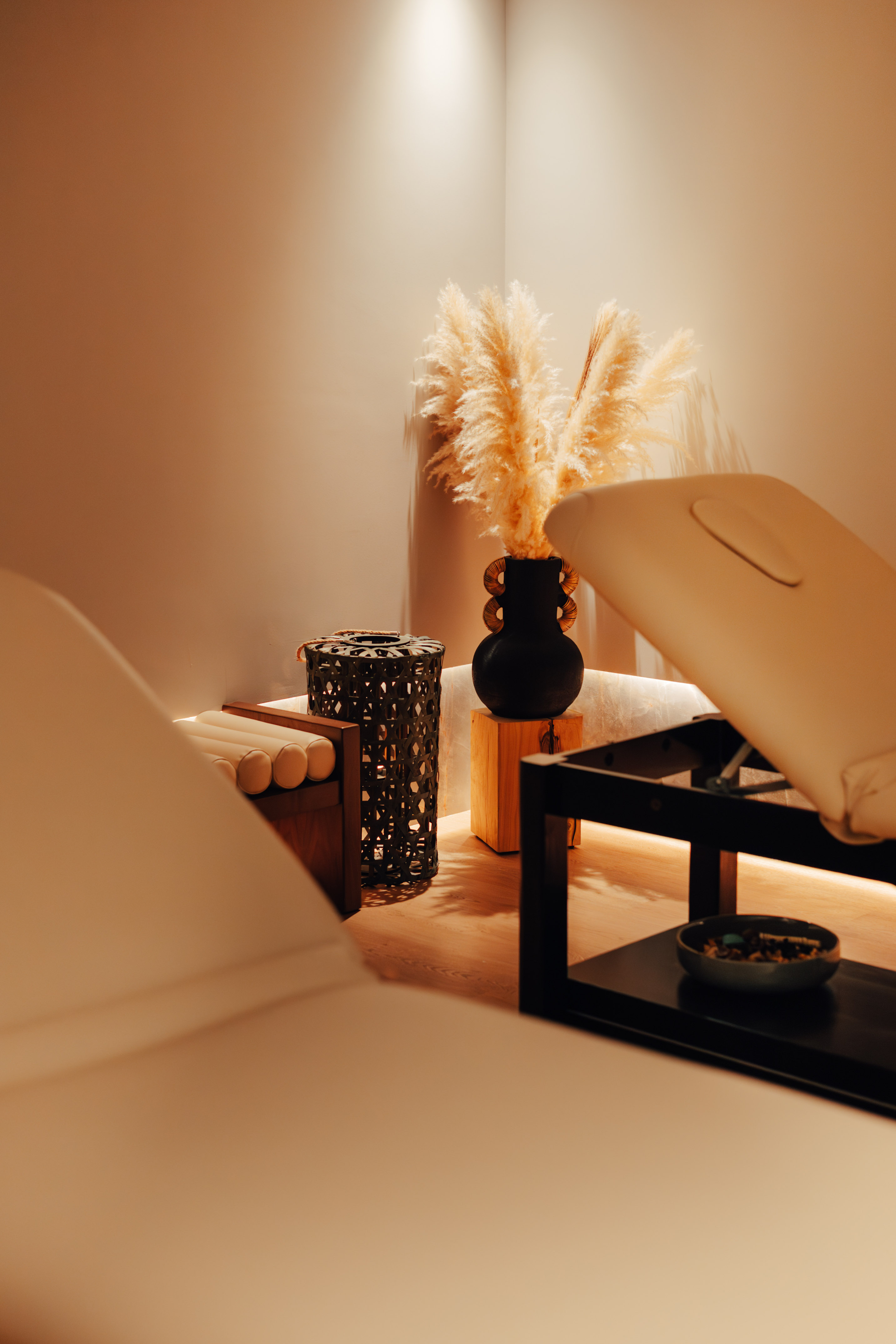 Warmly lit spa room with two massage beds and decorative pampas grass.